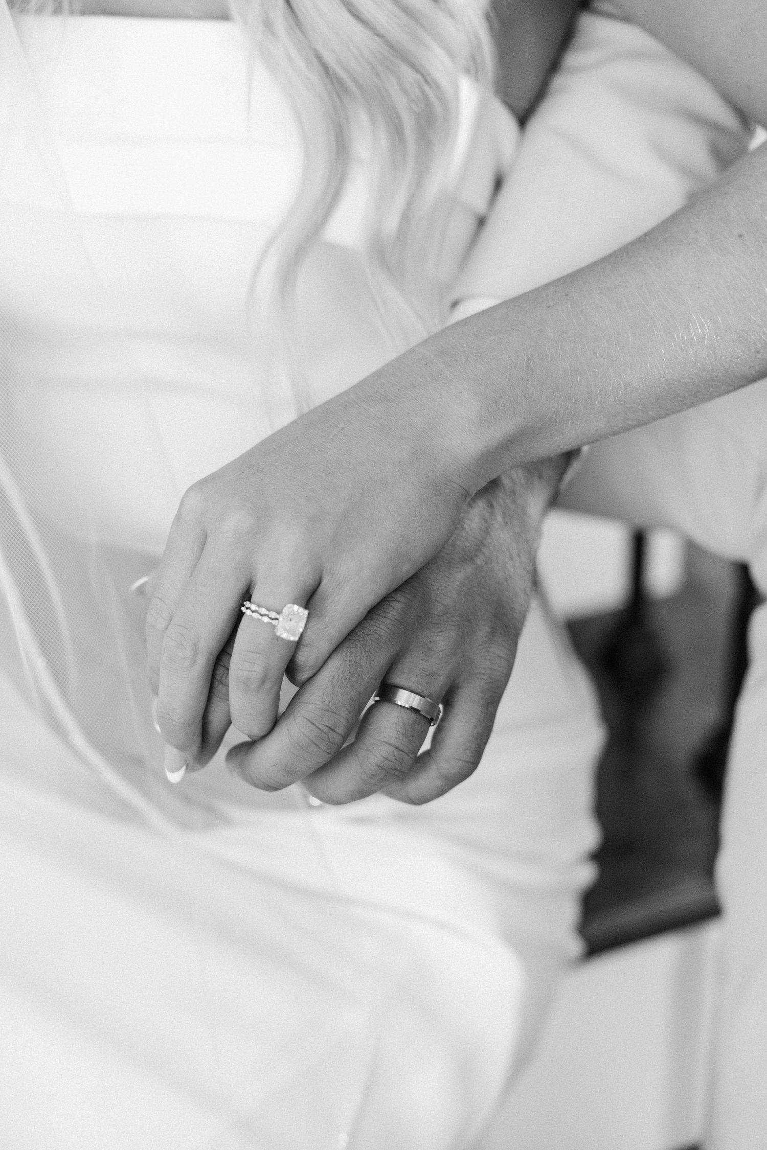 Black and white close-up of newlyweds holding hands showing wedding rings after ceremony.