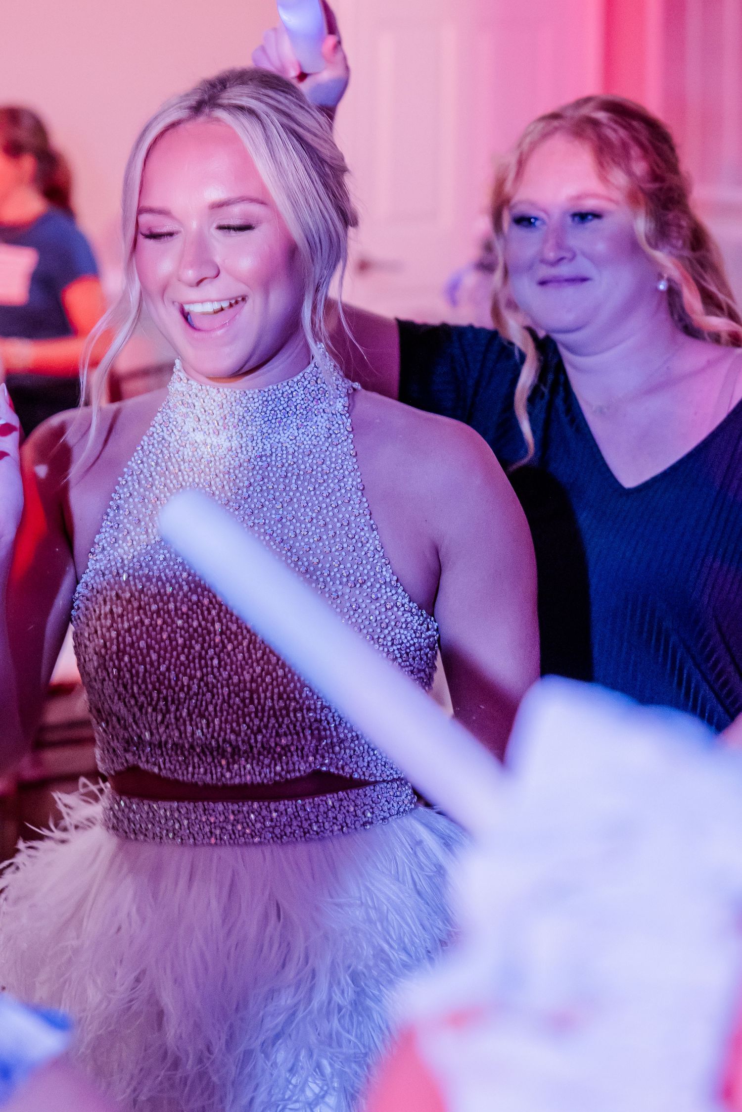 Bride in sparkling beaded crop top laughs joyfully while dancing at vibrant wedding reception.