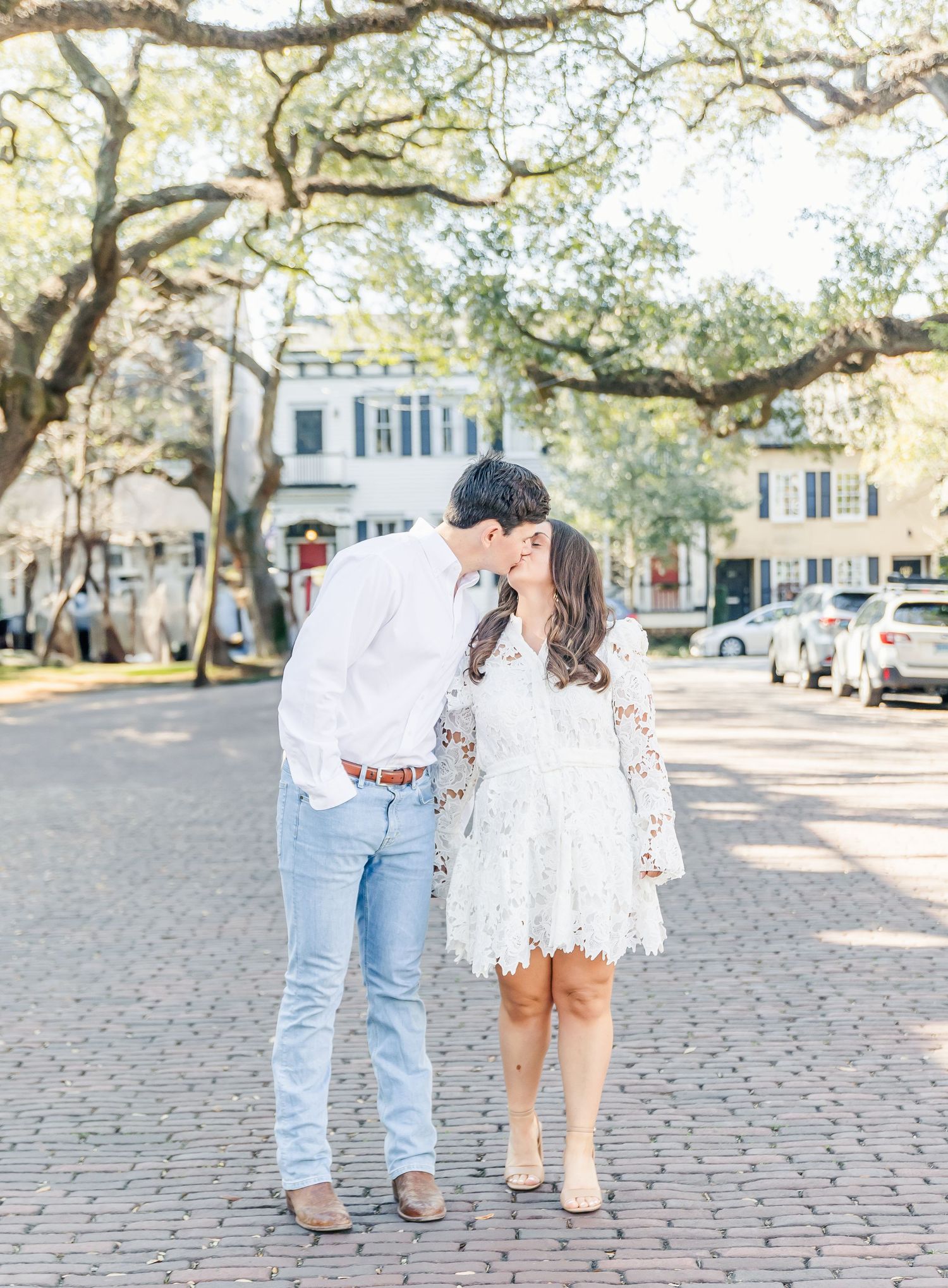 A tender moment between a couple on a tree-lined cobblestone street in Charleston.