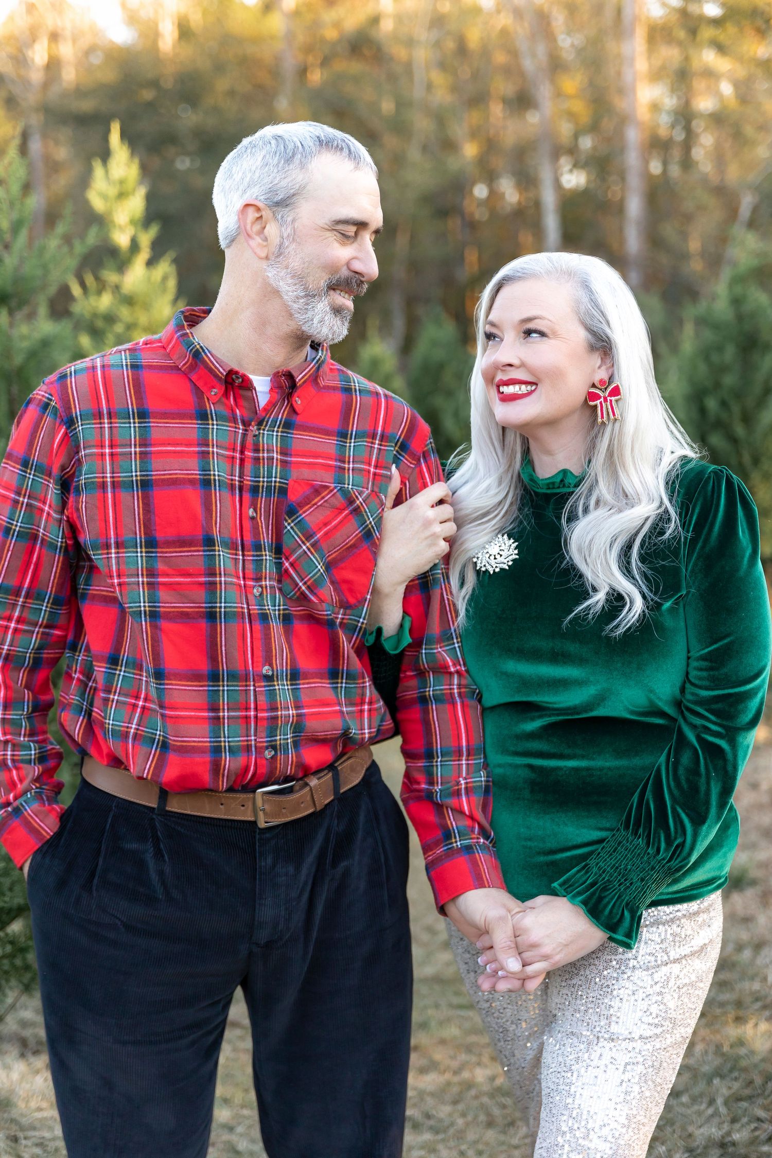 A festive holiday photo of a couple in plaid and velvet winter outfits outdoors.