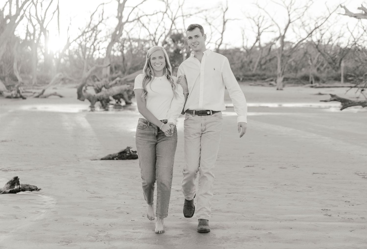 A couple walks together on a sandy beach in casual attire during golden hour.