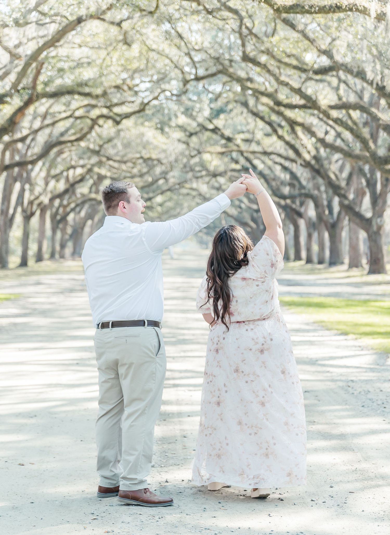 A couple dancing together on a tree-lined path in light spring attire.
