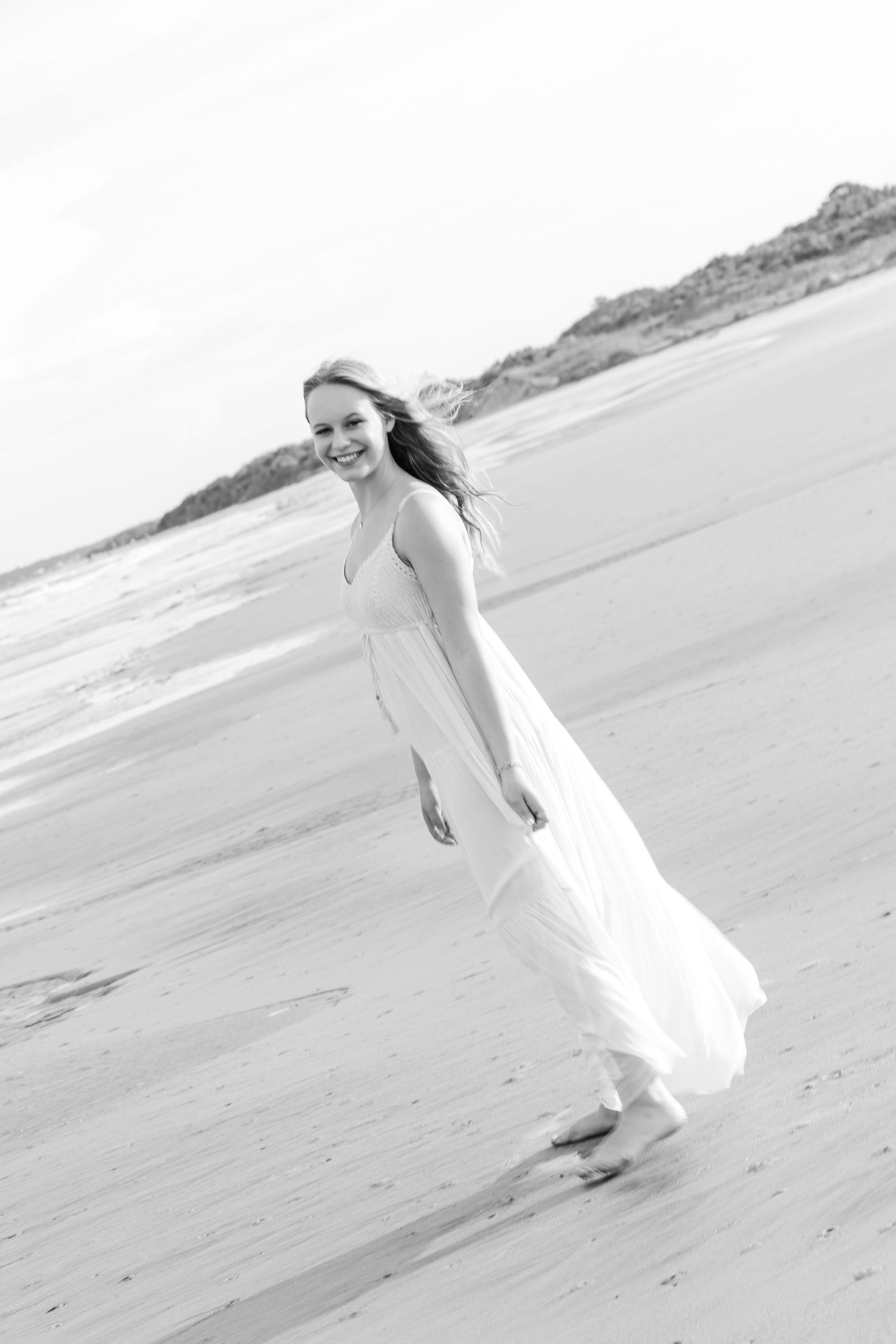 Artistic black and white series of a figure in white dress twirling on an empty beach.