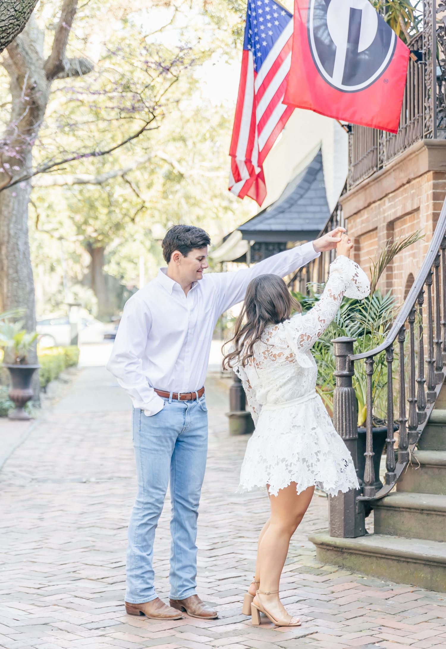 A romantic moment on a Charleston sidewalk with American flag and historic building in background.