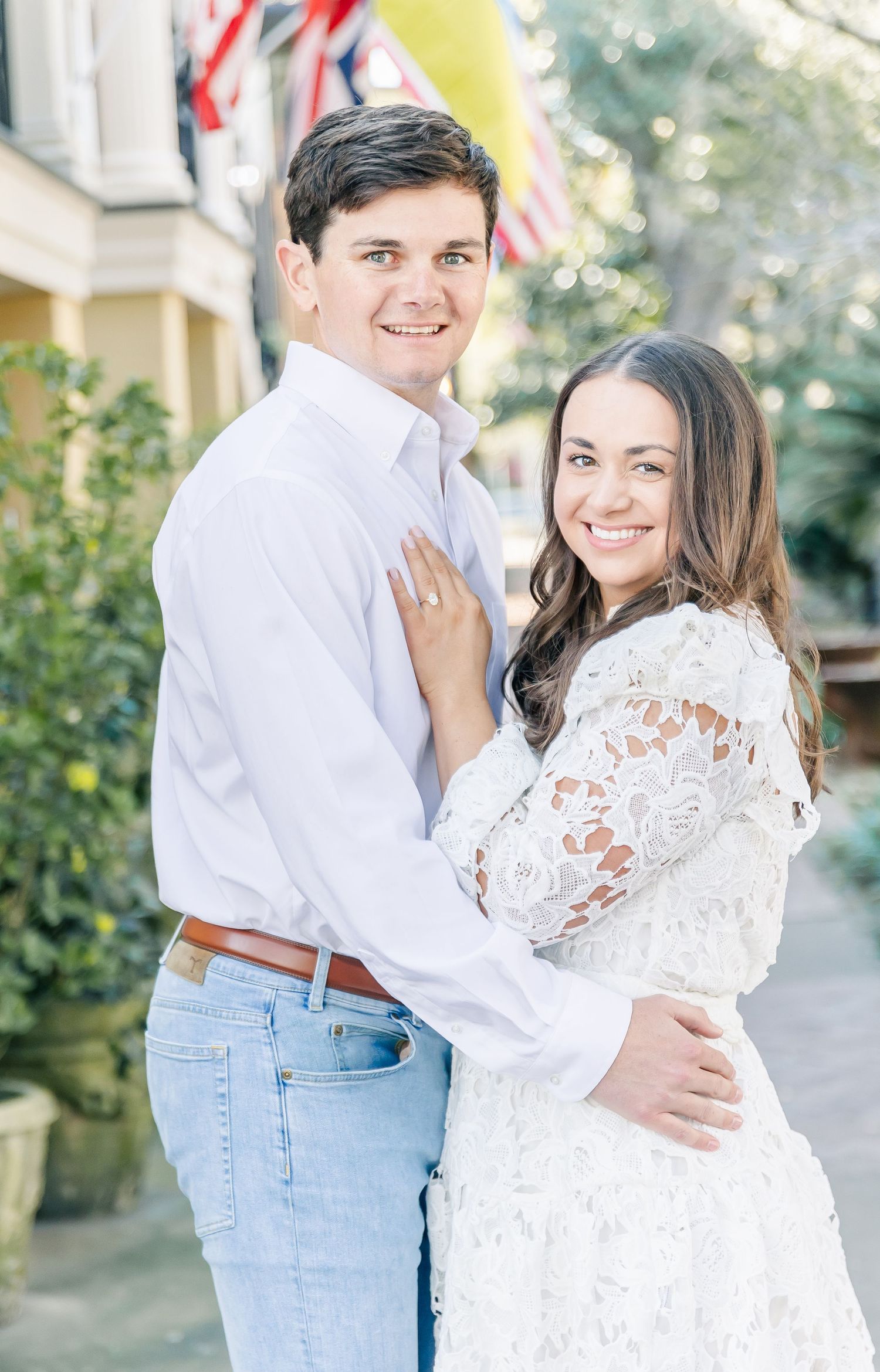A couple in white and jeans share romantic outdoor engagement photos with natural lighting and greenery.