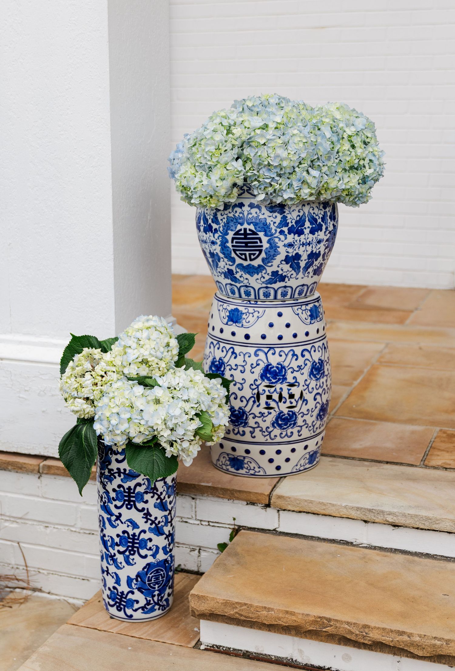 Blue and white chinoiserie vases filled with fresh hydrangeas displayed on stone outdoor steps.