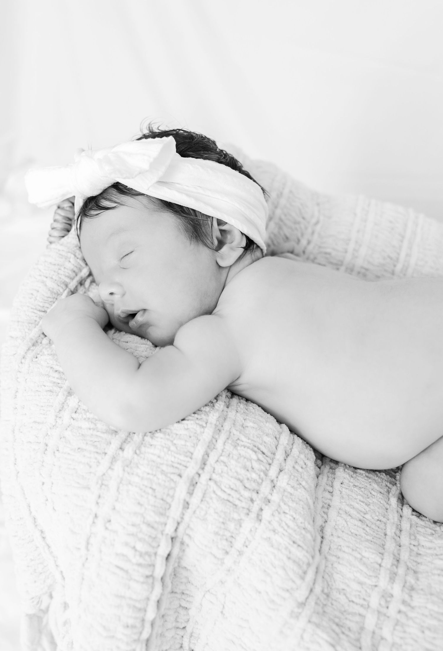 Side view of sleeping newborn with white headband on textured blanket.