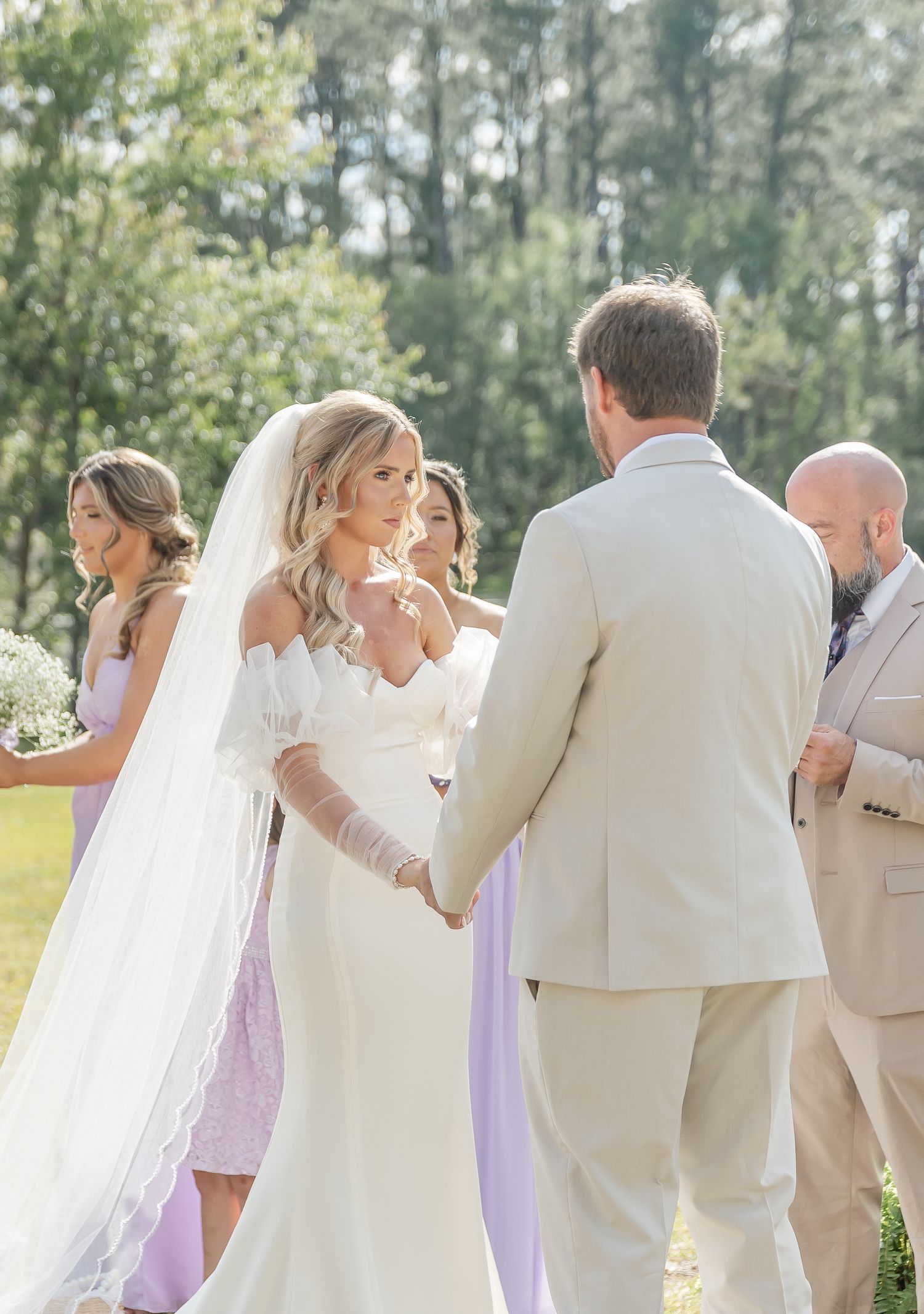 A sunny outdoor wedding ceremony with soft lighting and bridesmaids wearing flowing lavender gowns.