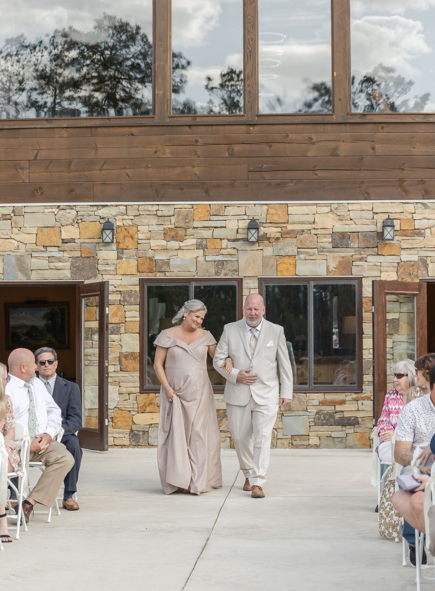 Formal procession at outdoor stone venue with guests seated in white chairs.