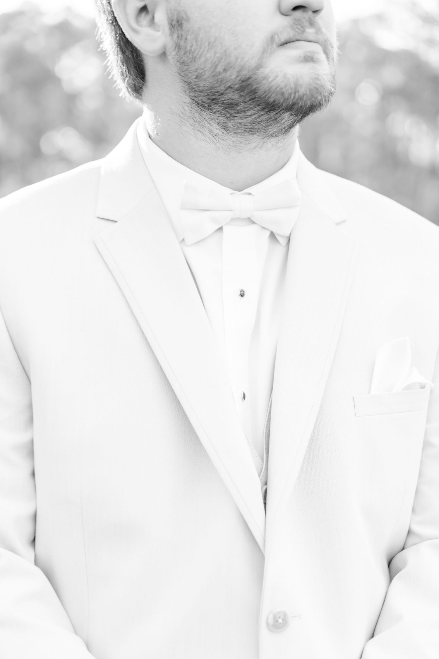 Close-up detail shot of groom wearing white tuxedo jacket and bowtie in black and white.