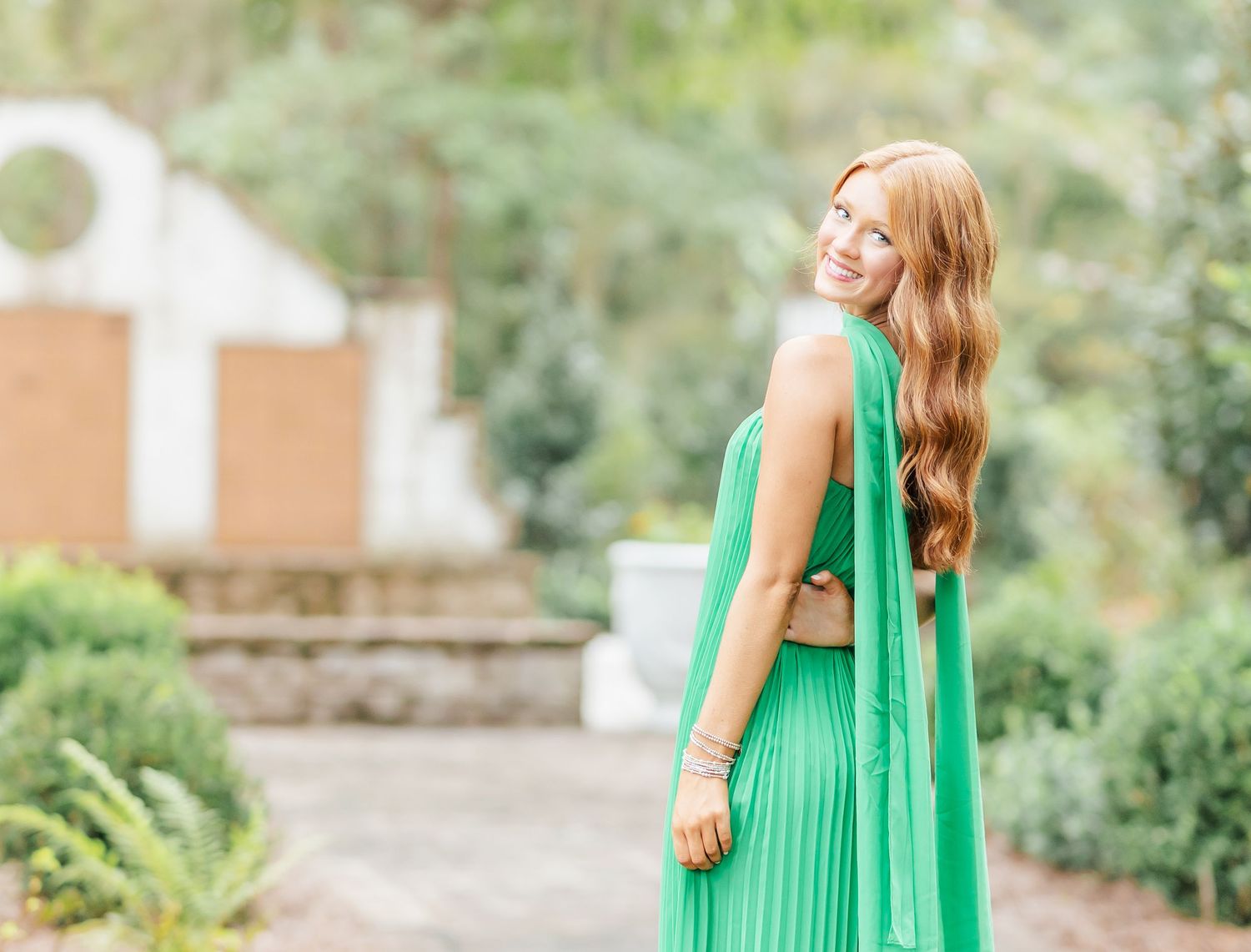 A person in a vibrant green pleated maxi dress poses against a garden background.