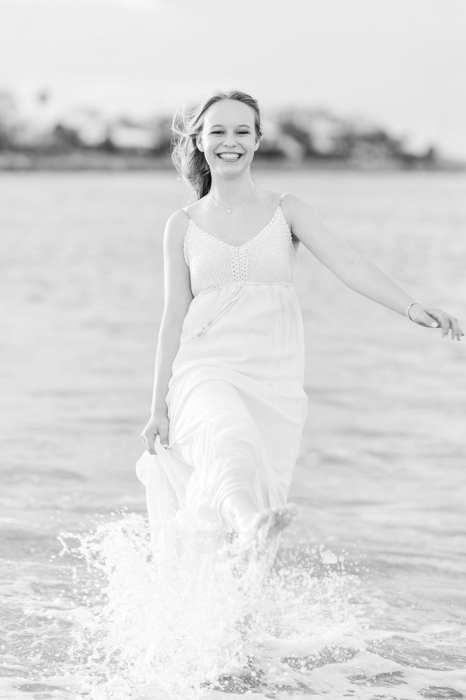 A black and white photo of a person joyfully splashing through shallow water in a flowing dress.