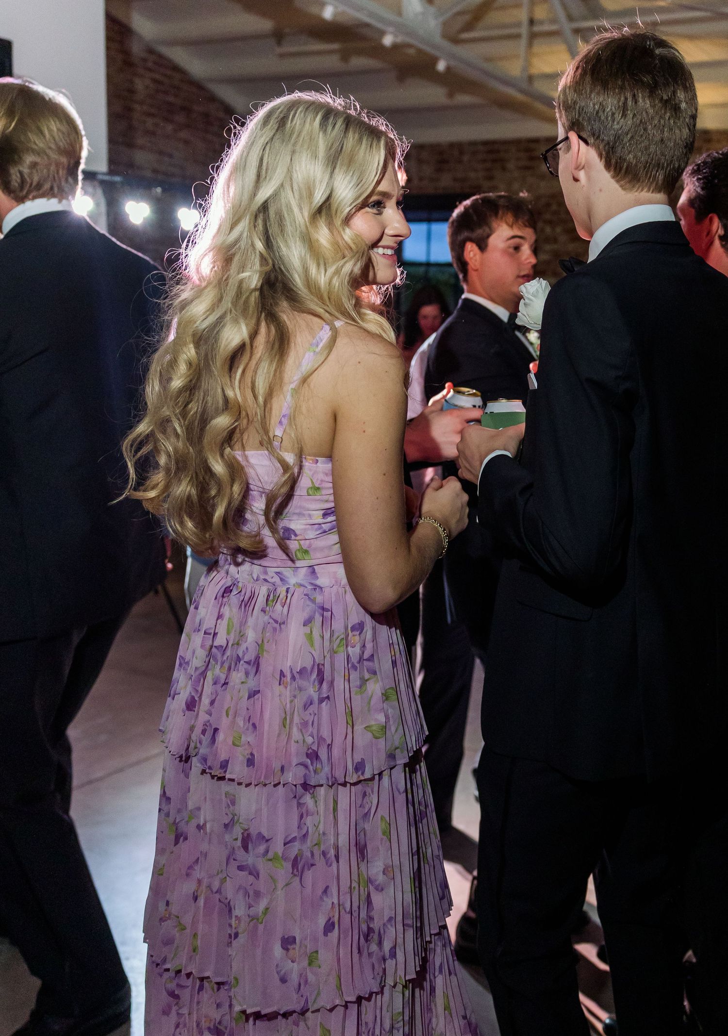 Guest in lavender floral dress with long blonde hair socializing at elegant wedding reception.