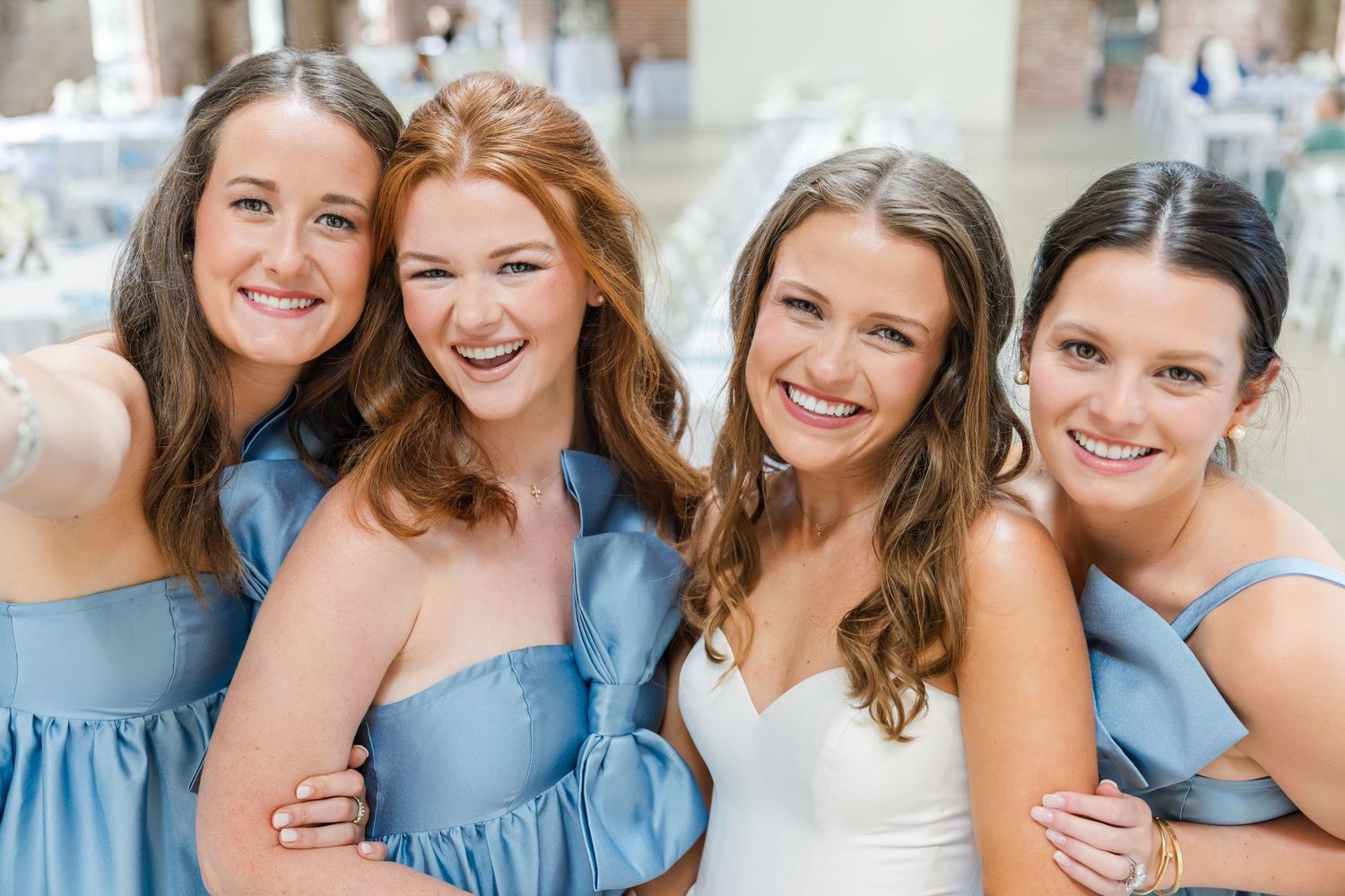 Bride in white gown posing with three bridesmaids in blue dresses smiling at wedding reception.