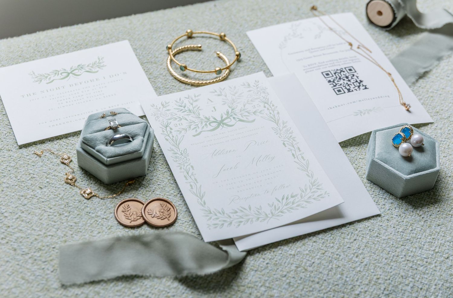 Flat lay of wedding stationery, rings, and gray hexagonal ring boxes on a textured white surface.