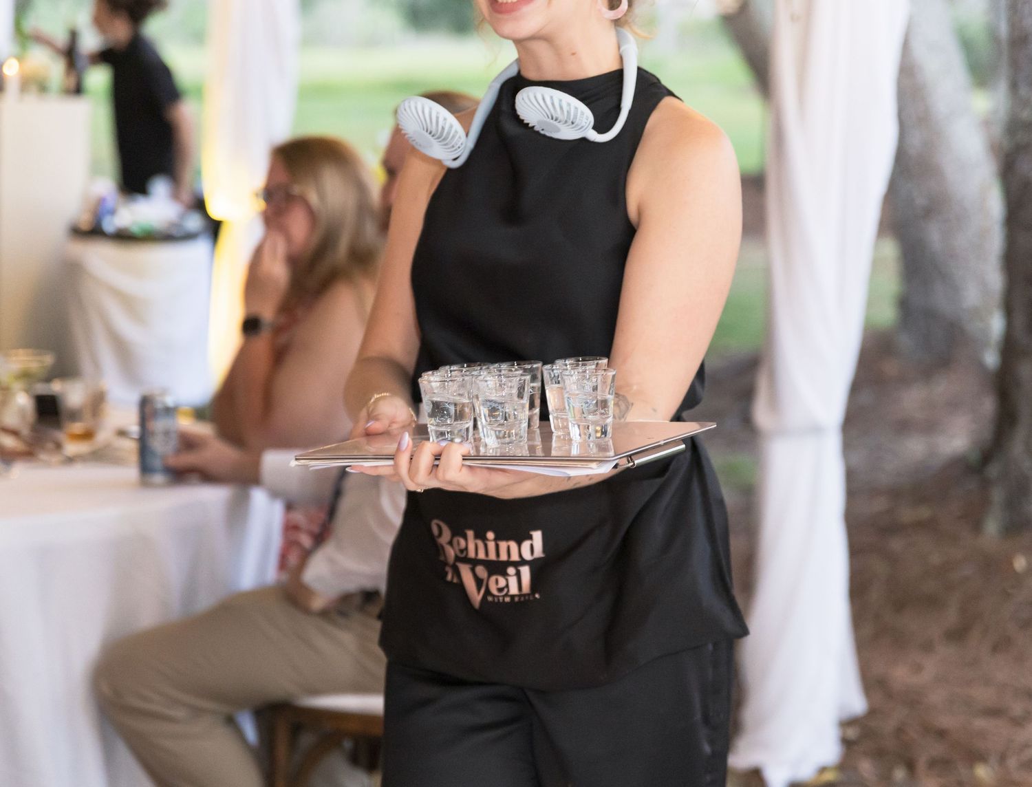 Guests enjoying refreshments and conversation at an outdoor catering event under trees.