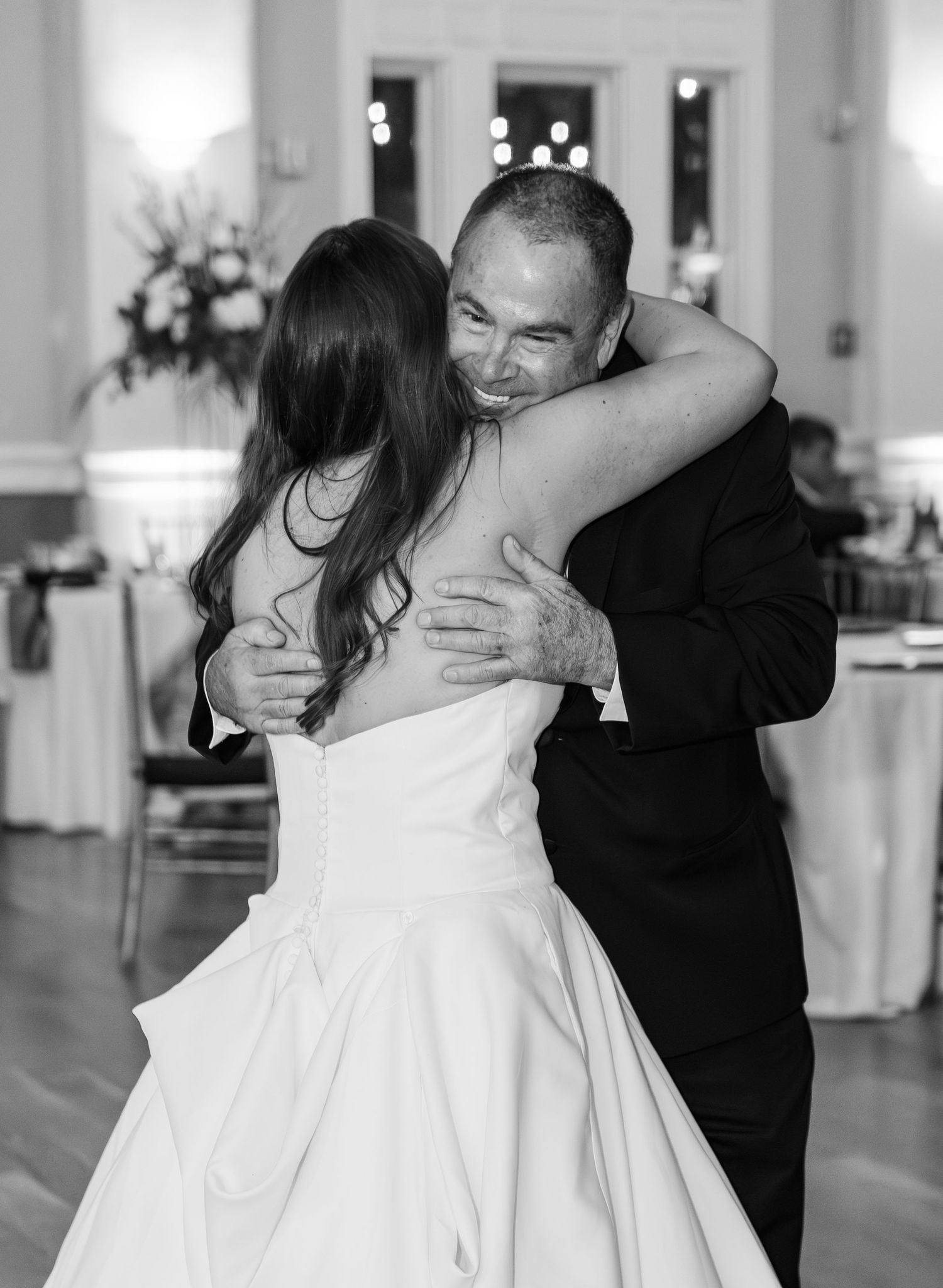 Black and white photo of a bride and groom sharing an emotional first dance hug at their wedding reception.