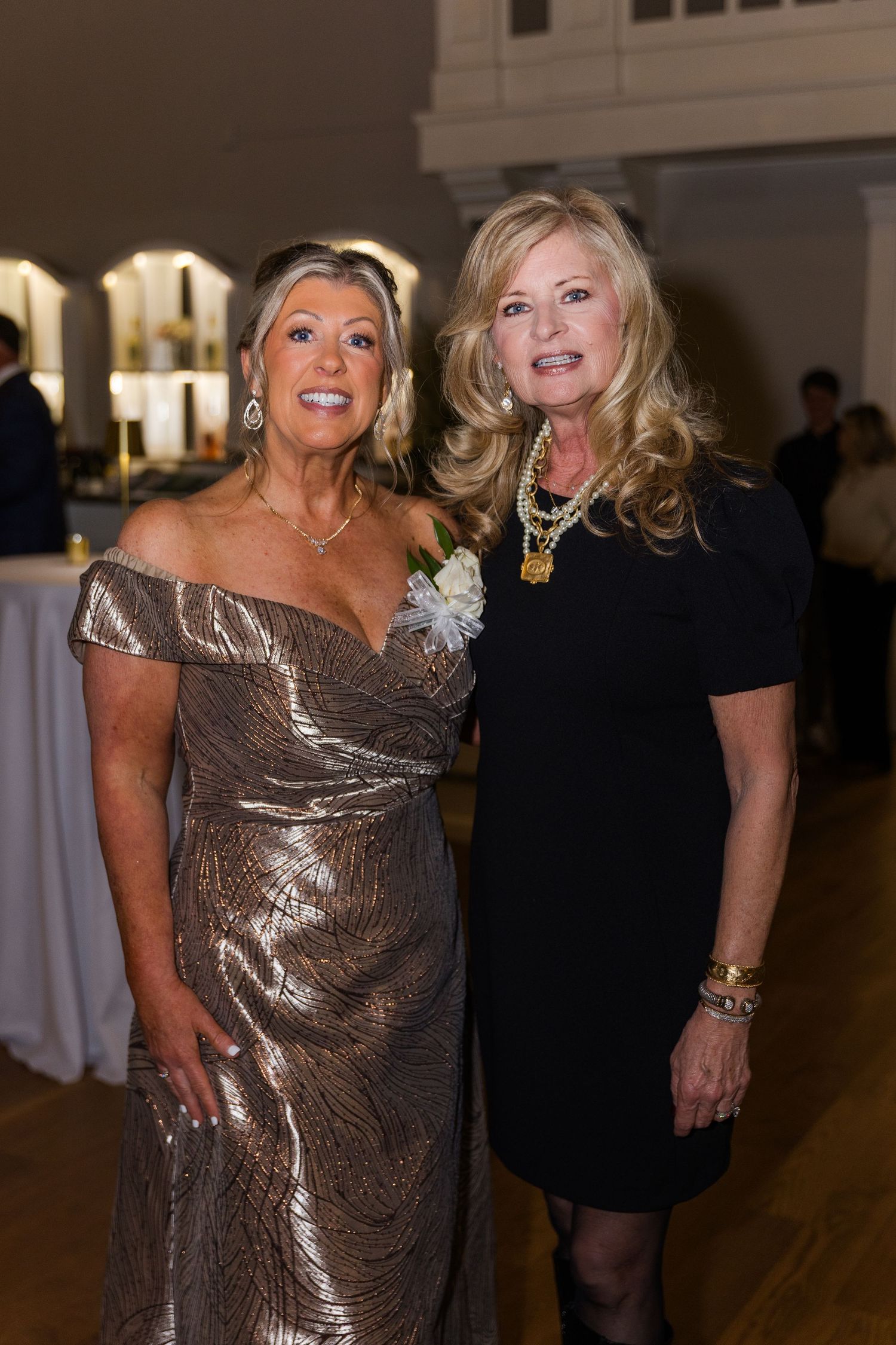Two elegantly dressed women pose together at a formal wedding reception event.