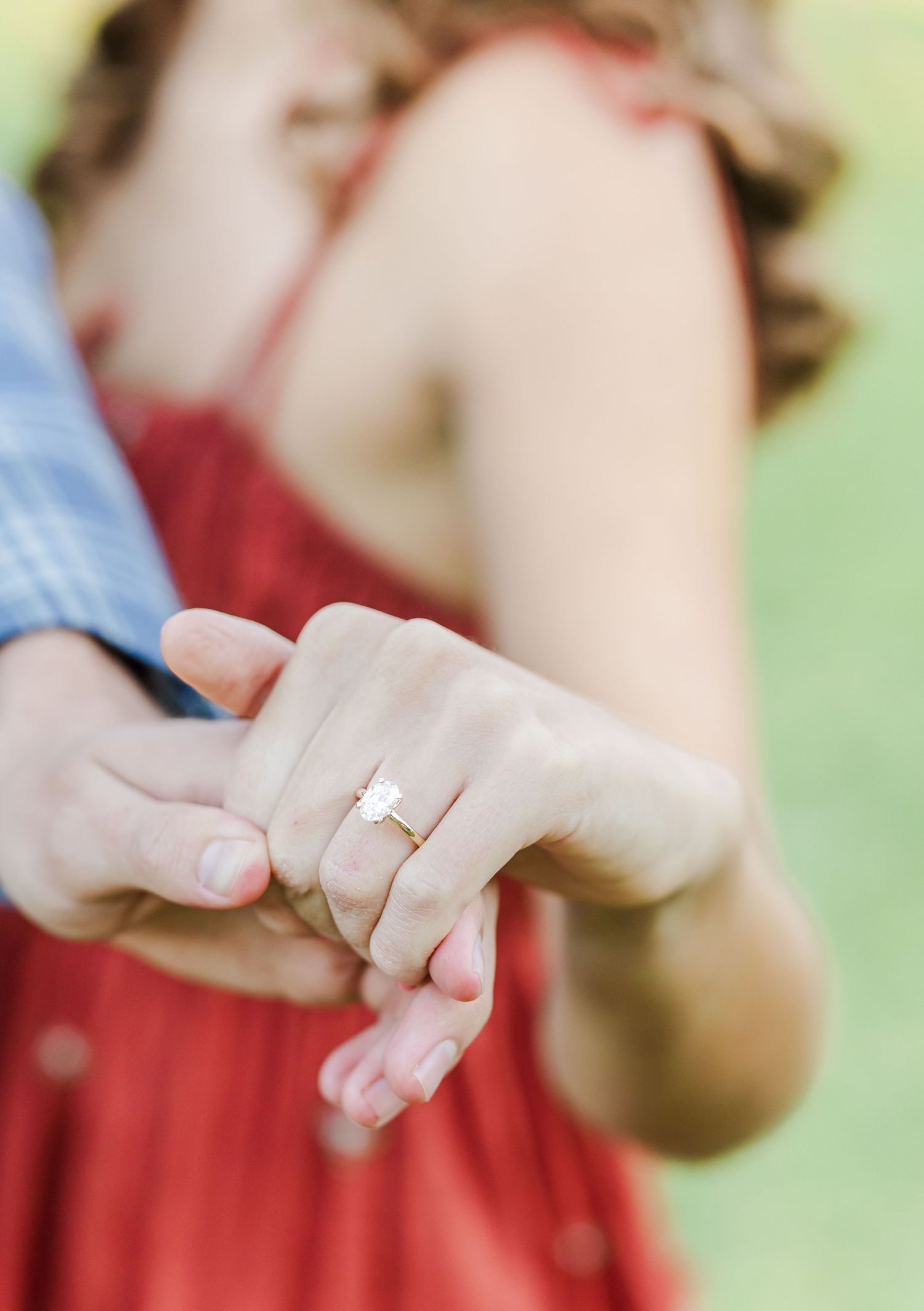 A delicate engagement ring sparkles on a hand against a soft blurred background.