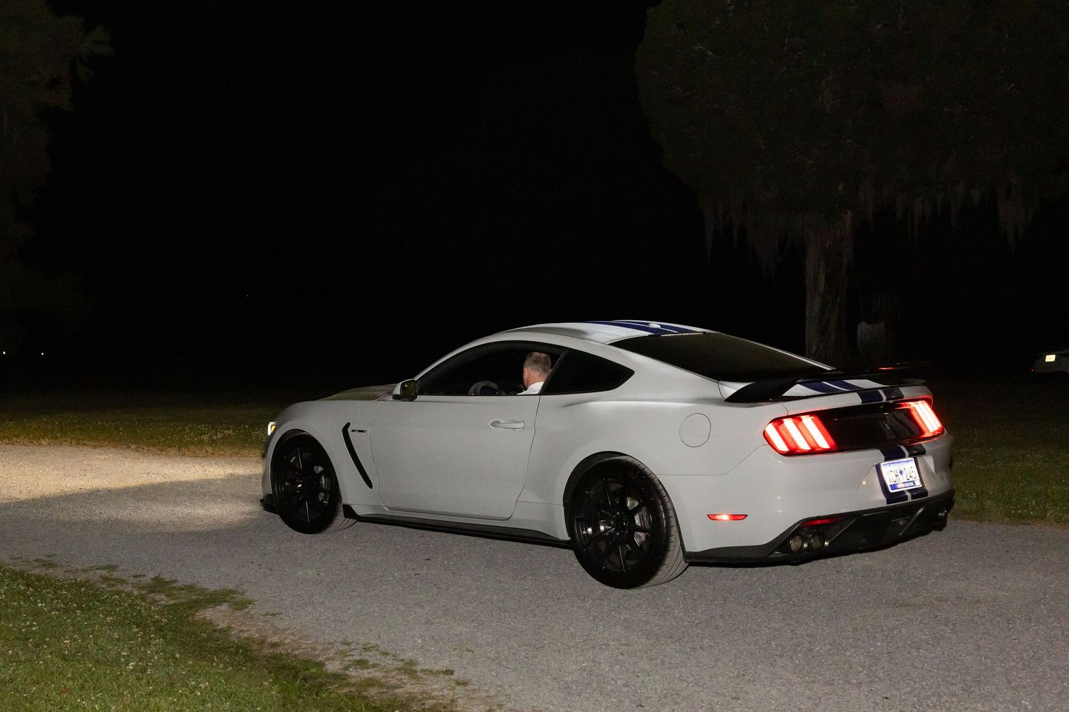 White Ford Mustang Shelby GT350 with black racing stripes parked on dark driveway at night.