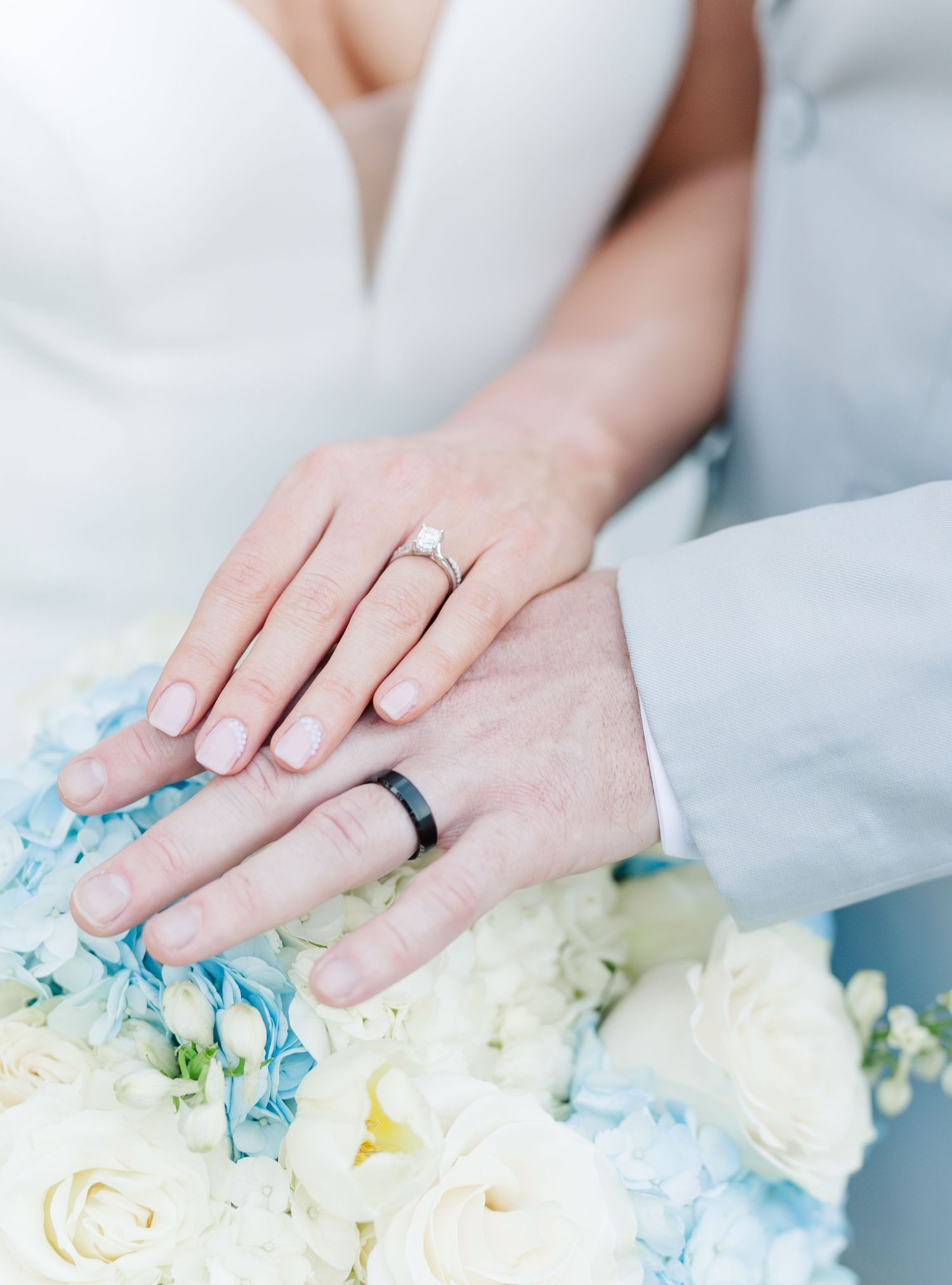 Bride and groom displaying wedding rings over a bouquet of white and blue hydrangeas.