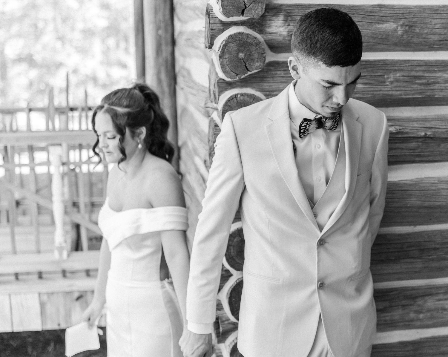 Black and white photo of bride and groom sharing a private first look moment at rustic log cabin.