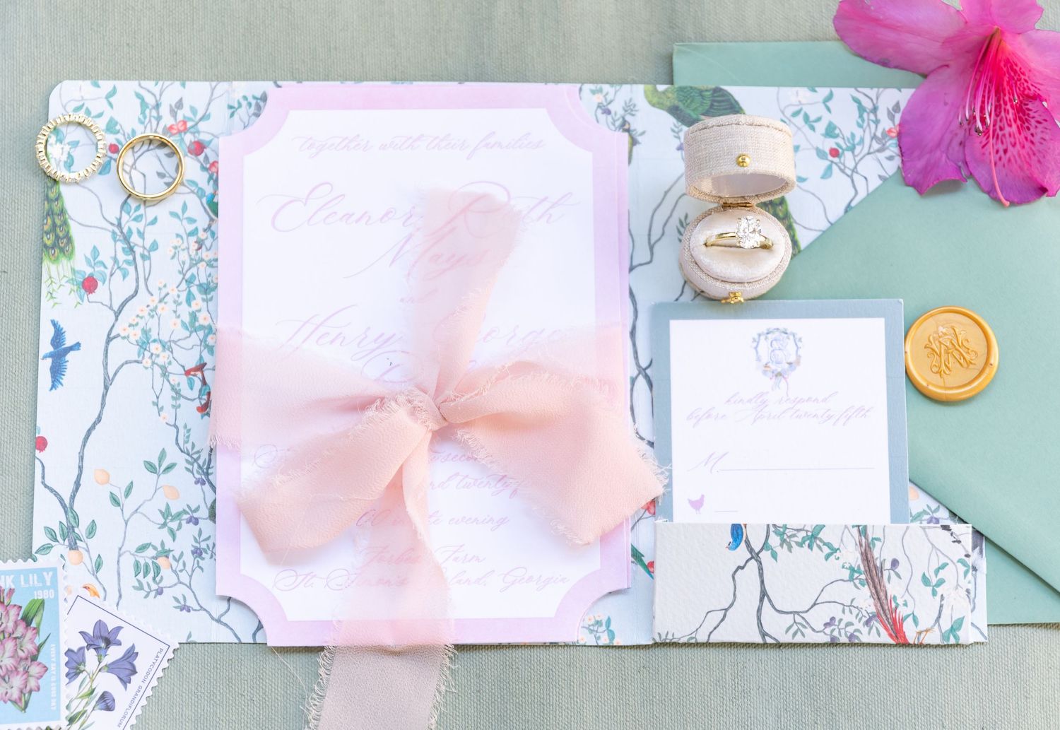 A wedding invitation with a soft pink bow displayed on a floral patterned background with small decorative elements.