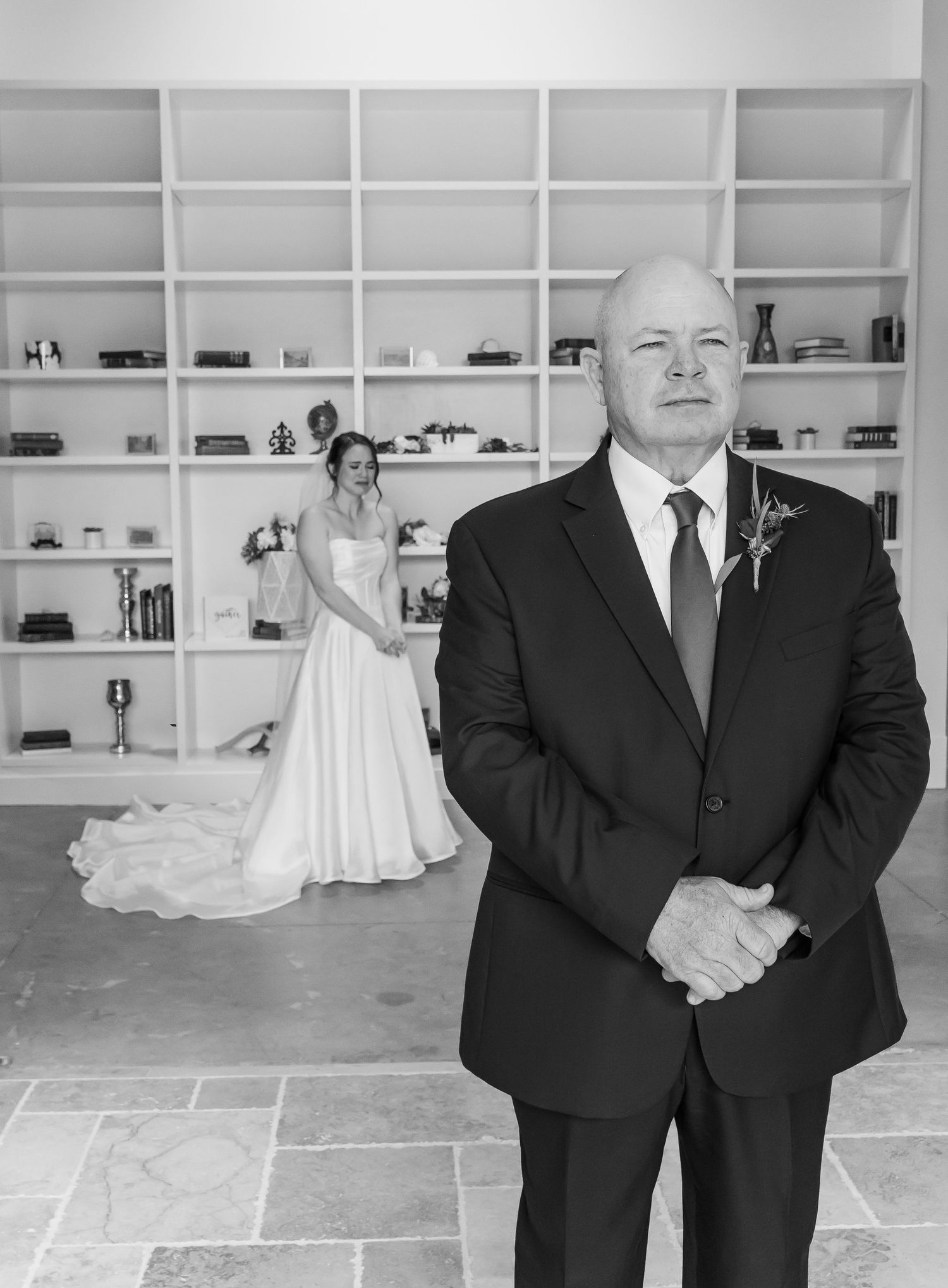 A touching pre-wedding moment captured in black and white showing a father and bride in a room with built-in shelving.