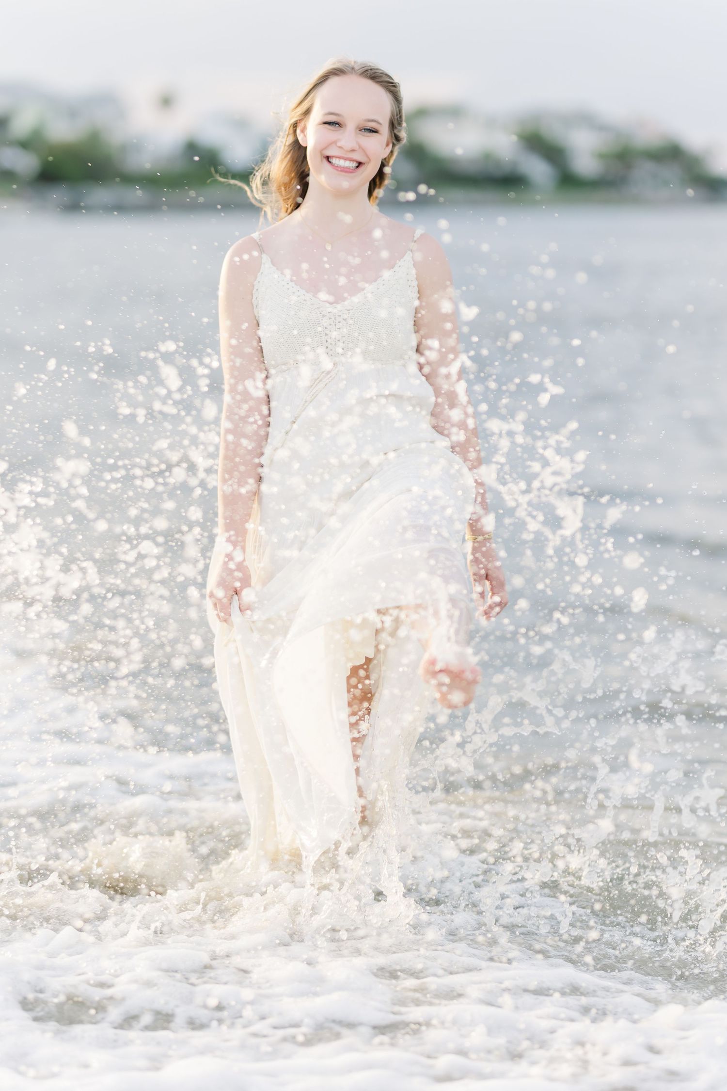 A person in a white dress splashing in ocean waves during a beach photoshoot.