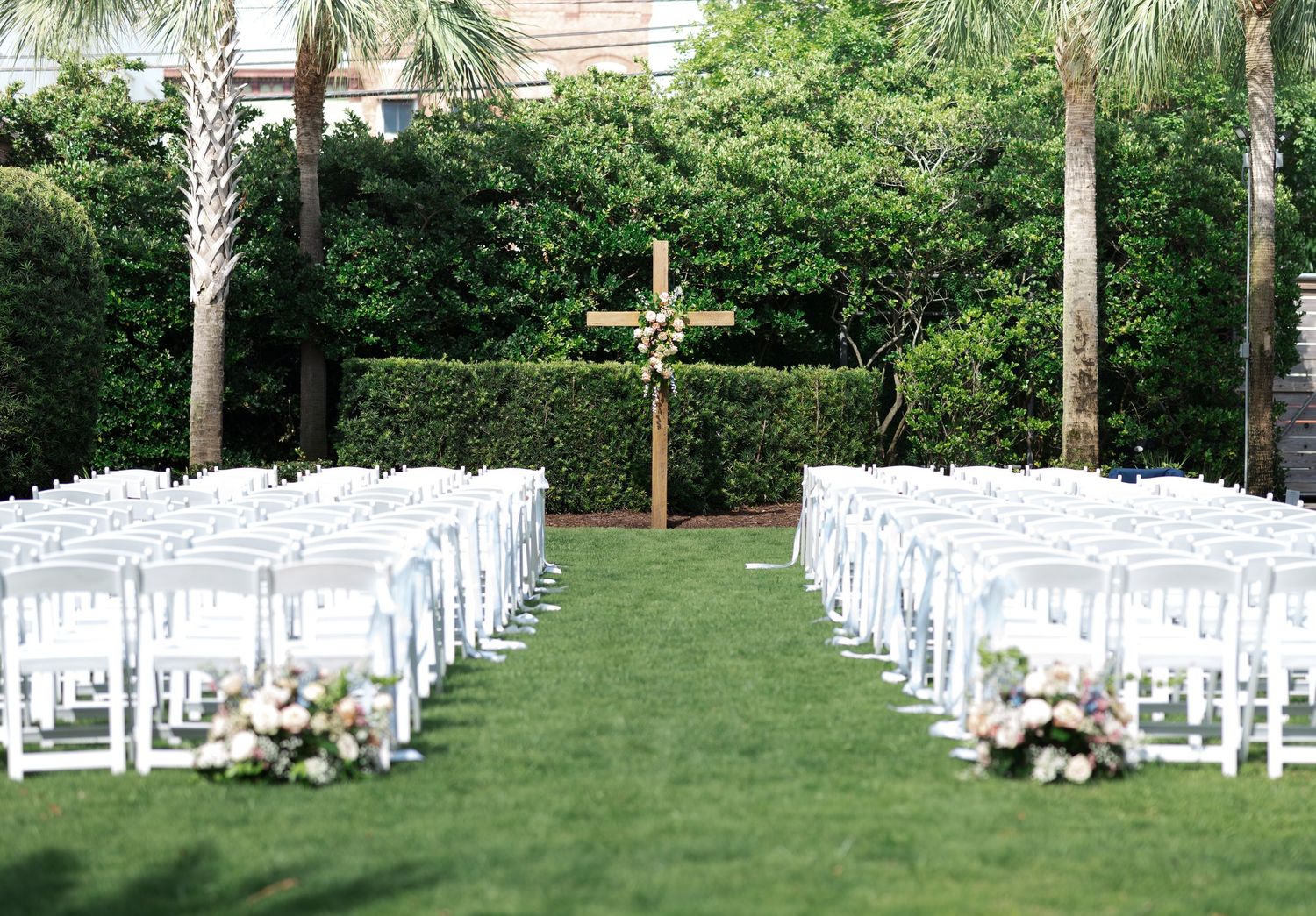 White folding chairs arranged in rows on a green lawn for an outdoor wedding ceremony with palm trees in the background.