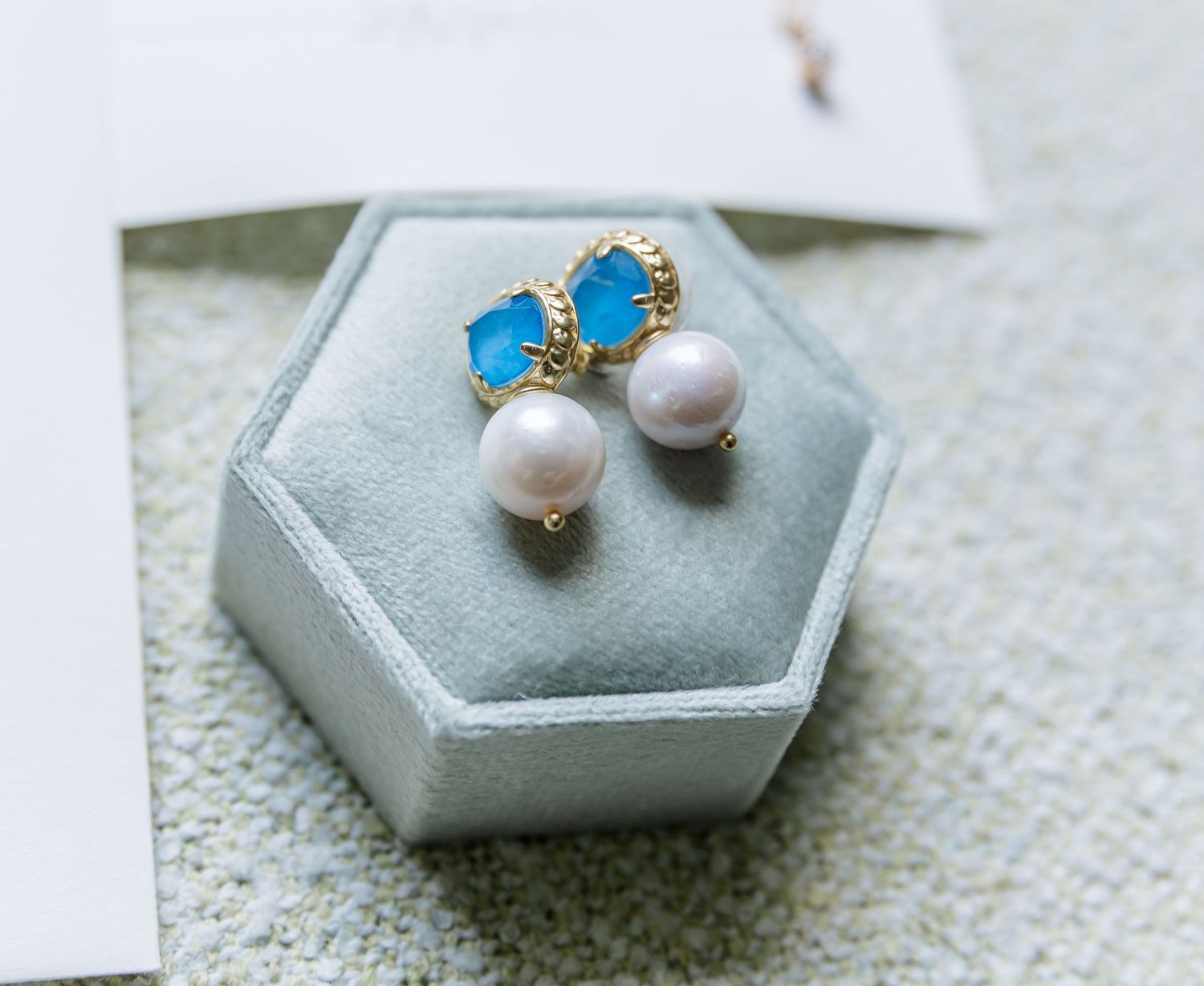 Delicate pearl and turquoise butterfly stud earrings displayed on hexagonal gray display stands.