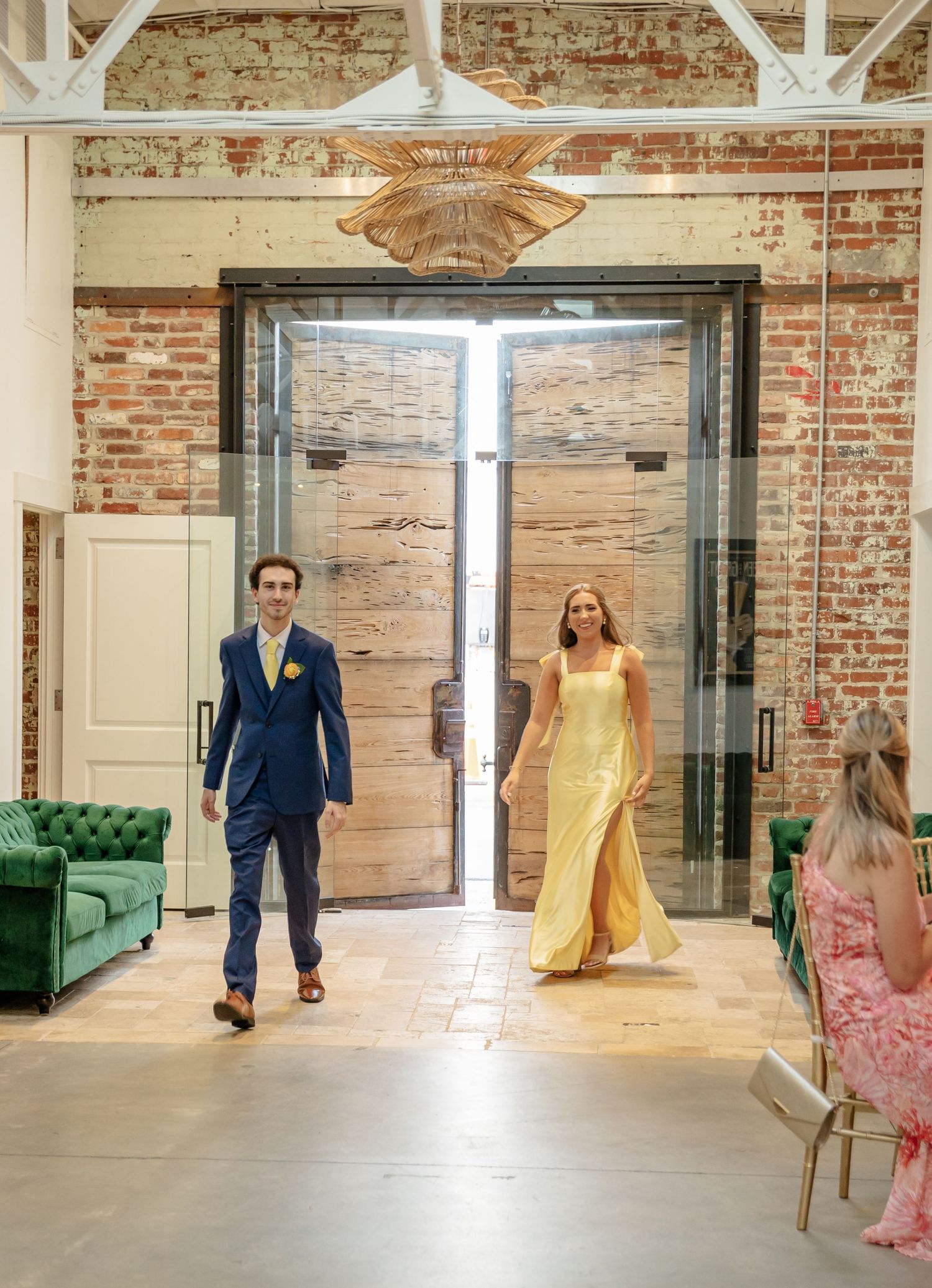 Wedding party members in formal attire dance and twirl in an industrial brick venue with white beams.