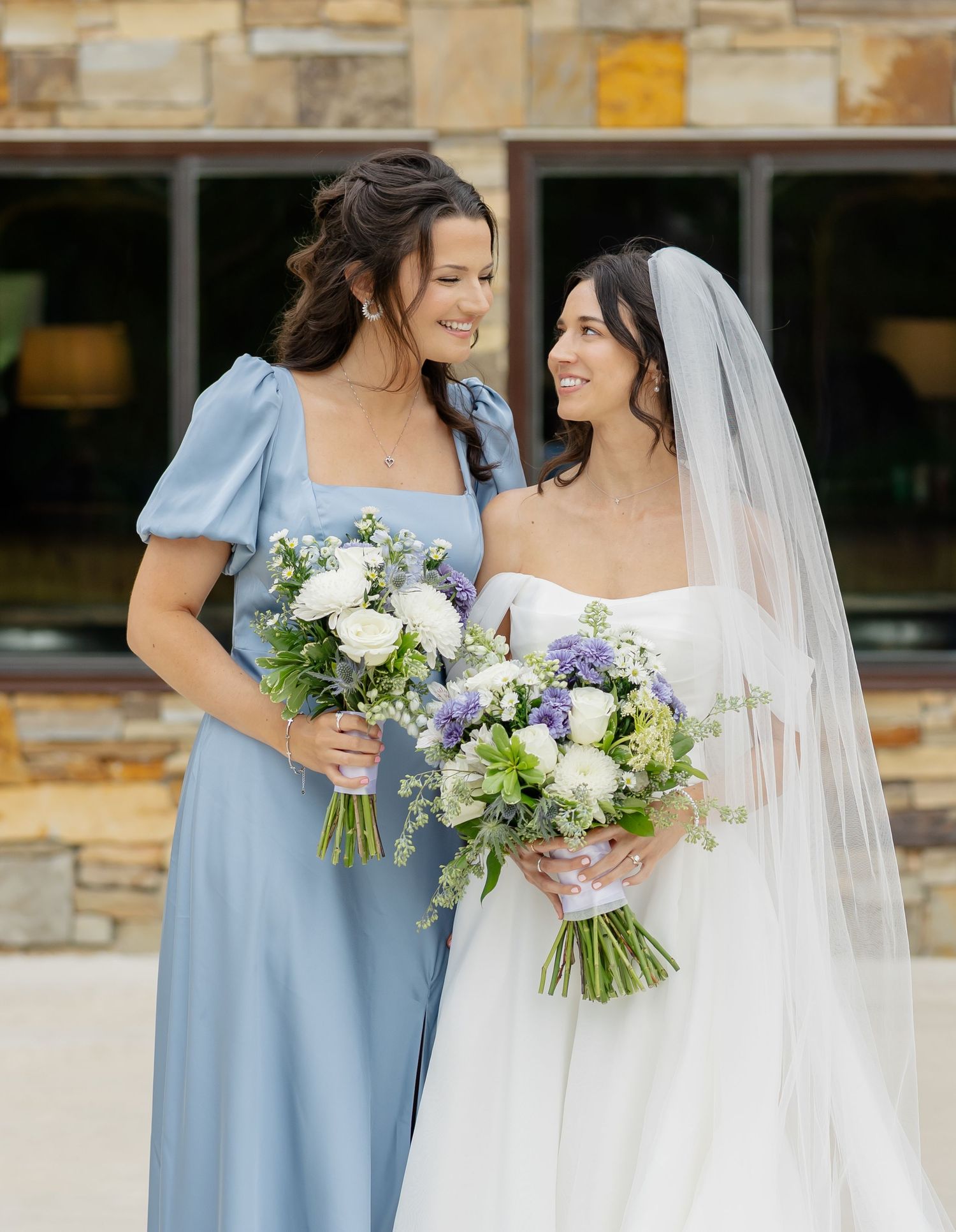 Bridesmaids in powder blue dresses stand with bride in white gown holding pastel flower bouquets.
