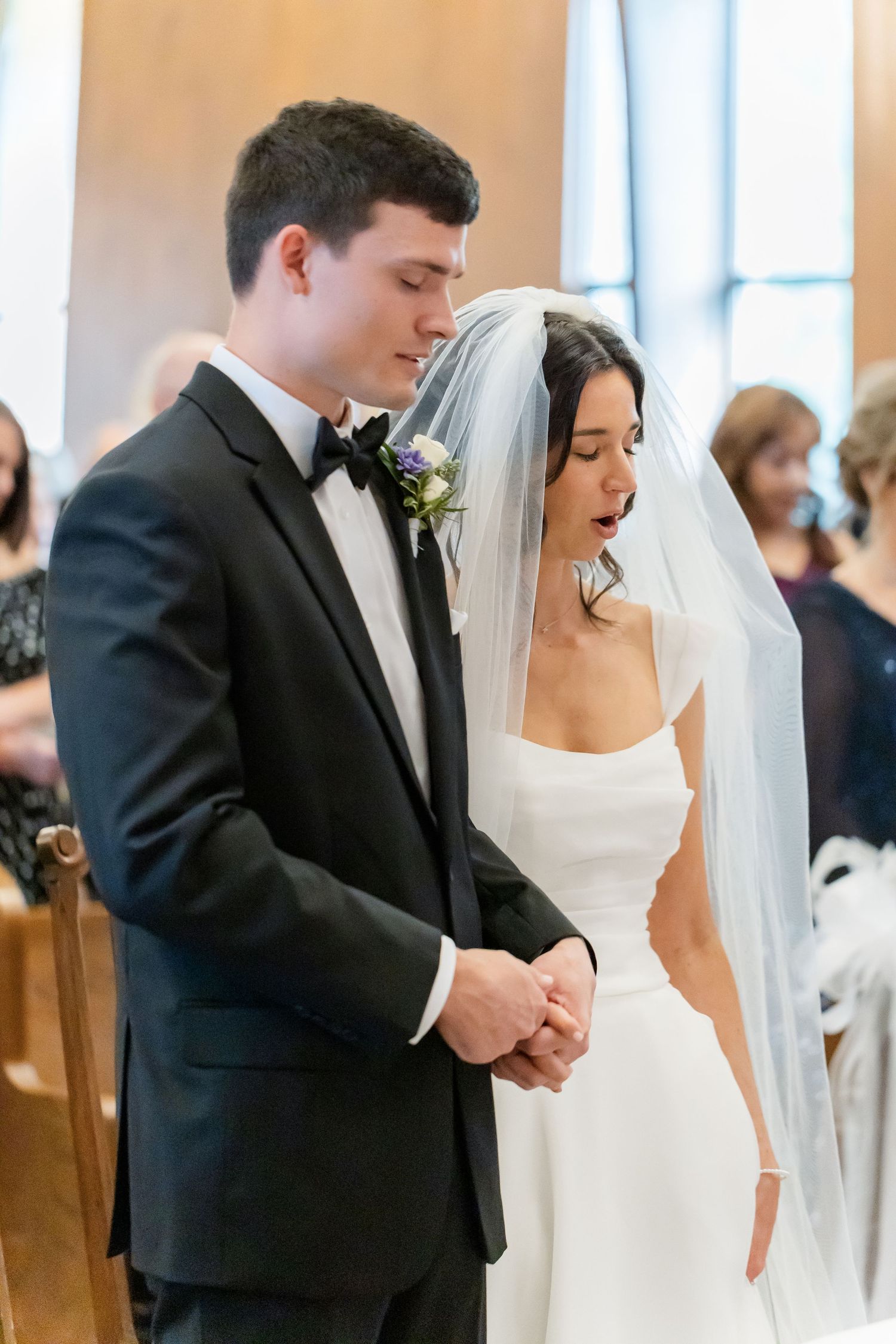 A bride and groom share an emotional moment during their wedding ceremony in a sunlit church.