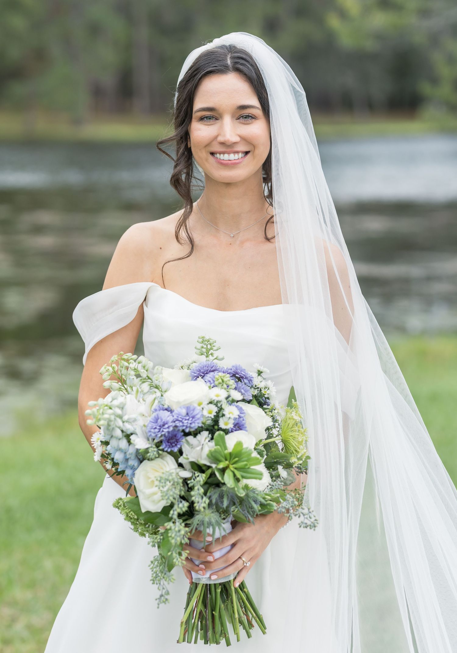 A bride in a white wedding dress holds a beautiful bouquet of purple and white flowers with cascading greenery.