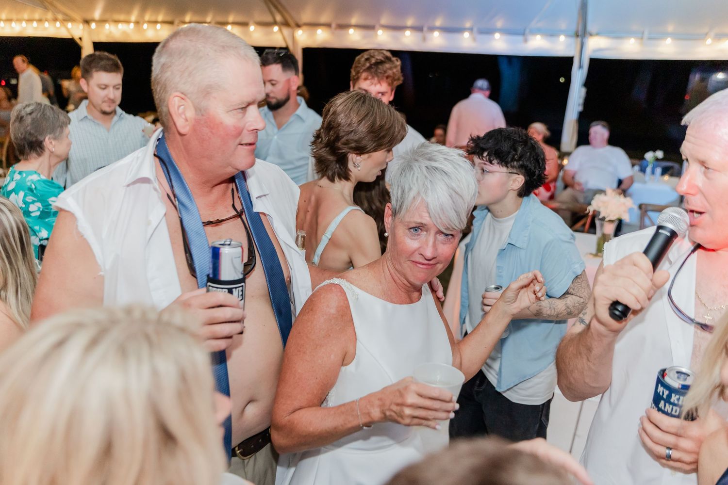 Wedding guests enjoy drinks and conversation during an outdoor reception celebration at sunset.