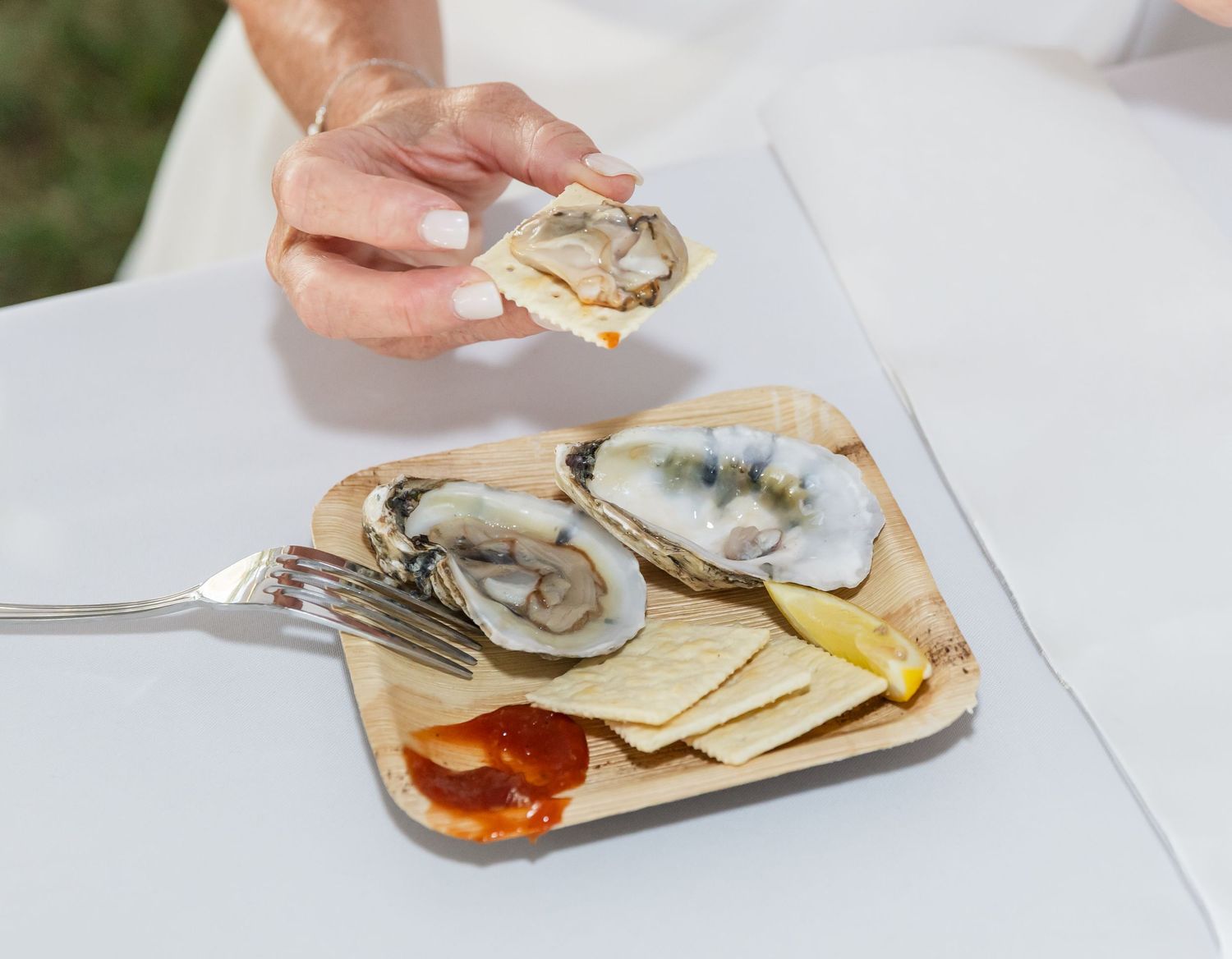 Fresh oysters being shucked and served with mignonette sauce on a white surface.