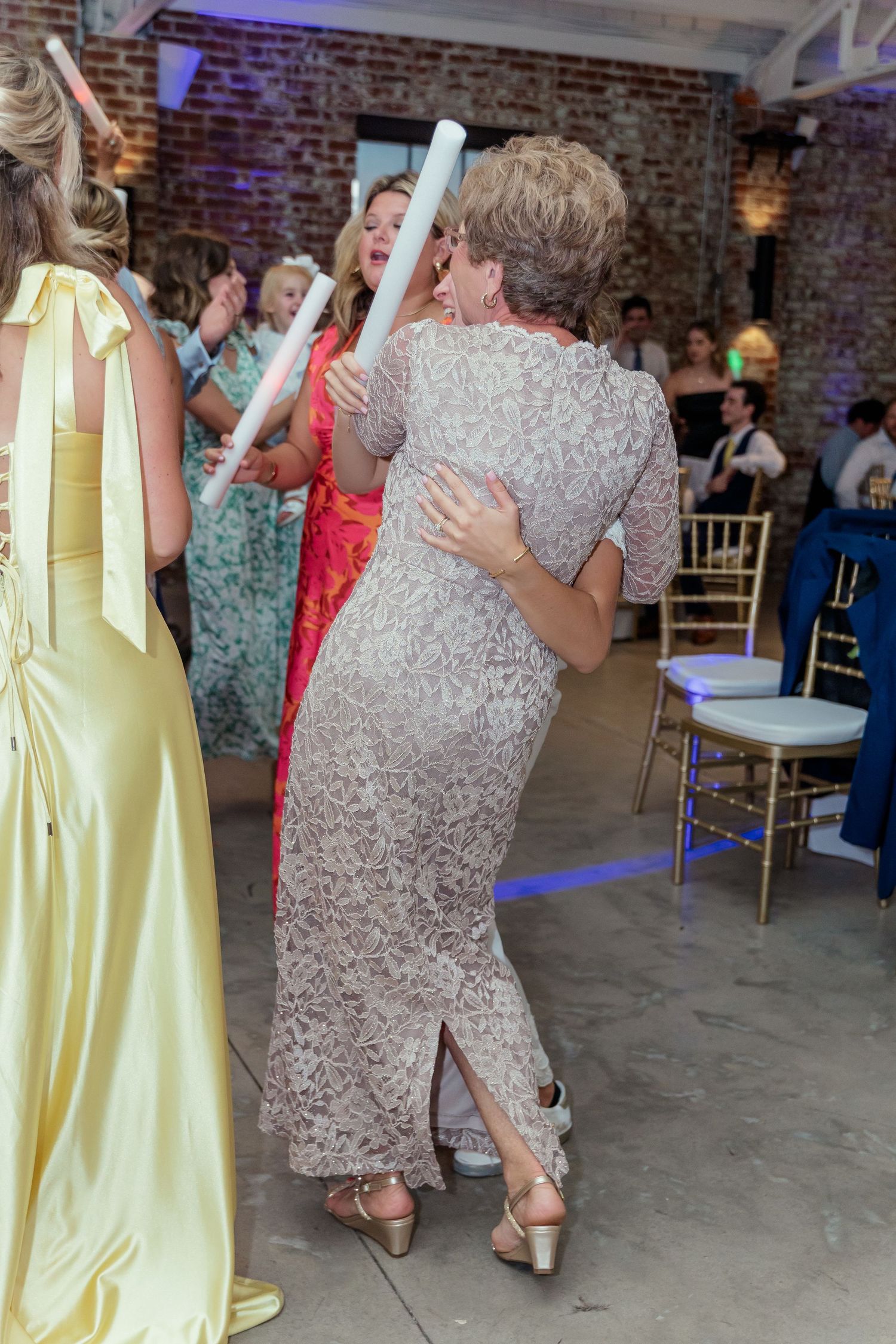 Couples dancing together in an industrial-style venue with exposed brick walls and yellow dresses.