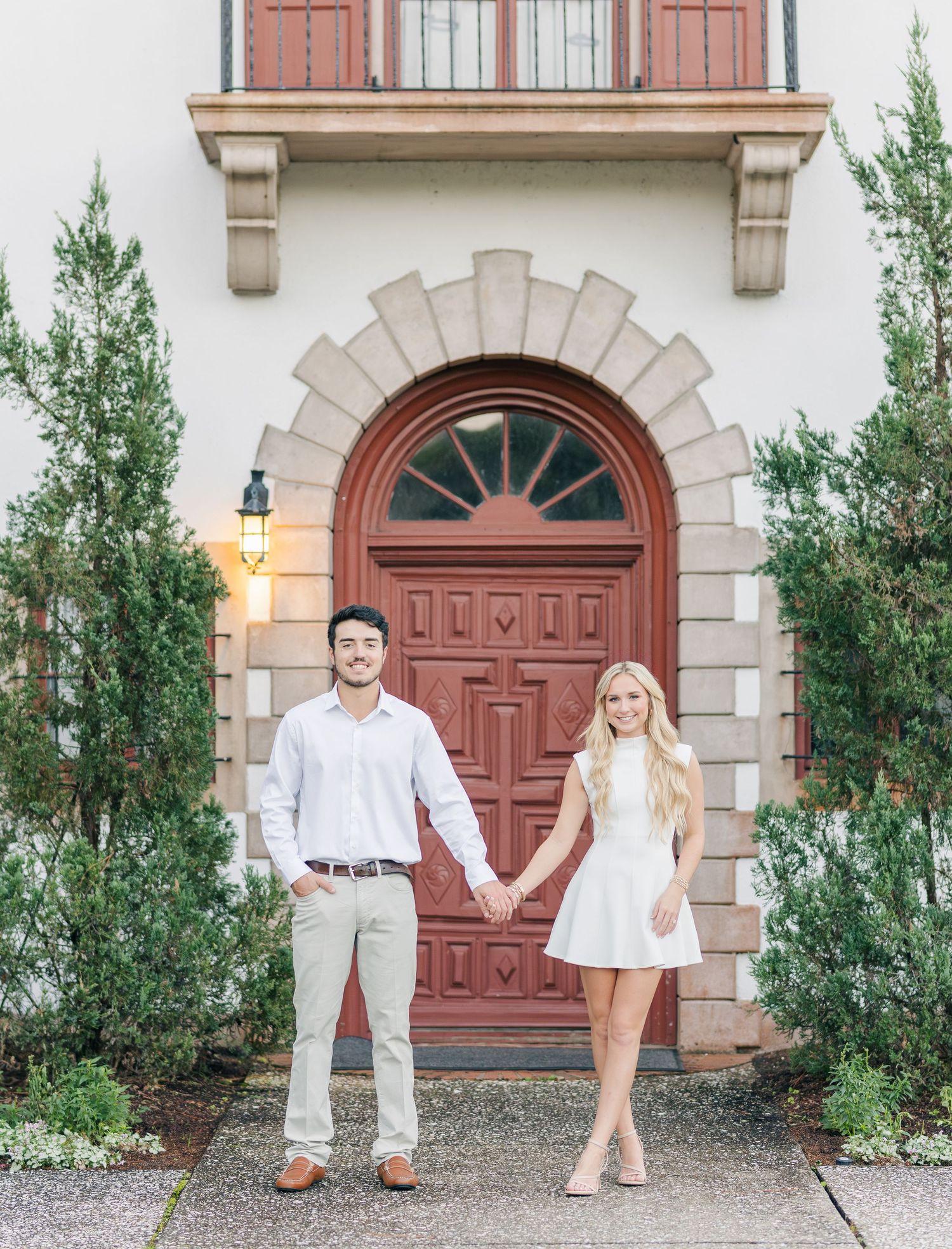A couple poses for romantic engagement photos in front of an ornate wooden door and stone archway entrance.