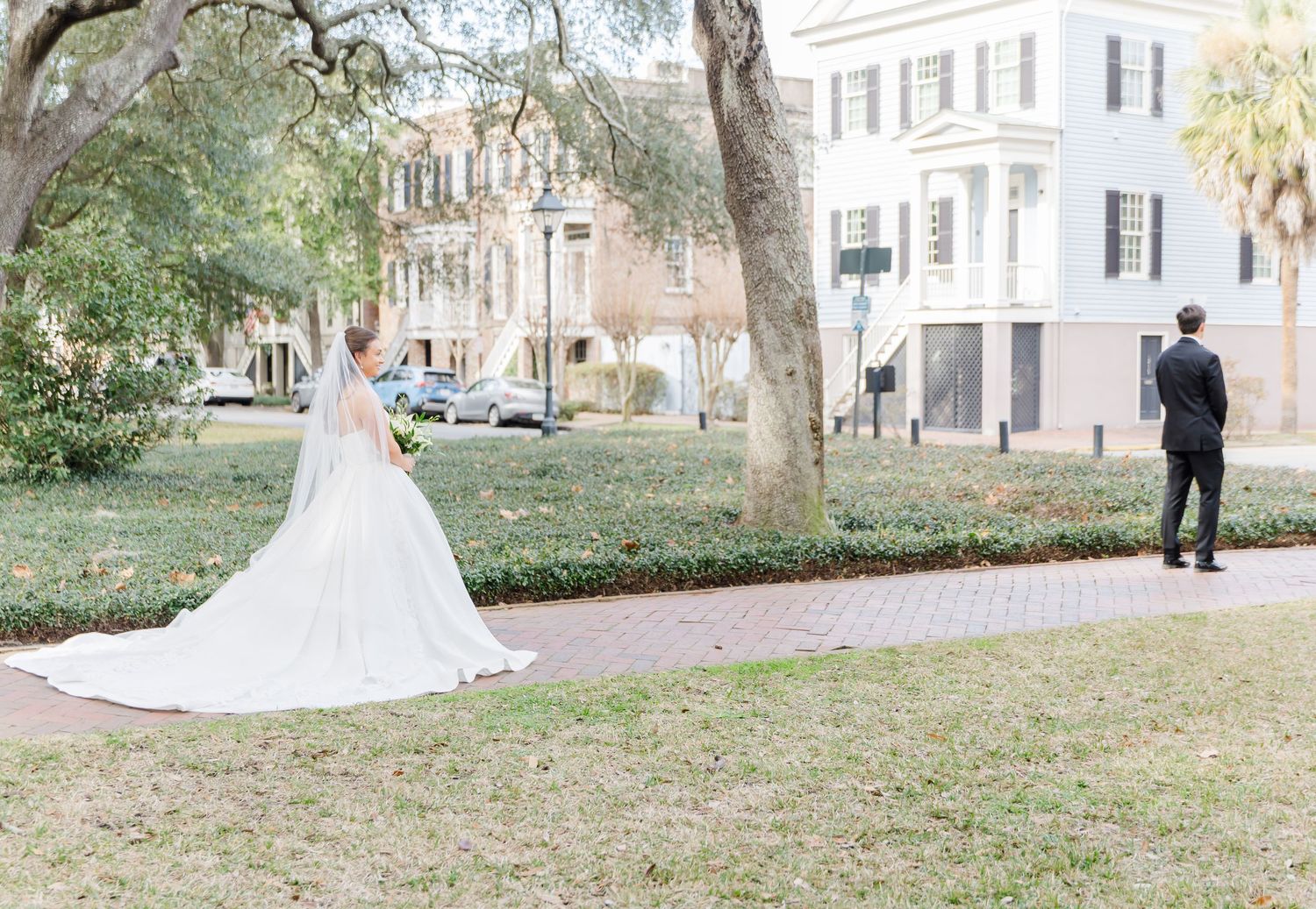 A bride in a flowing white wedding gown poses gracefully in a scenic Charleston garden setting.