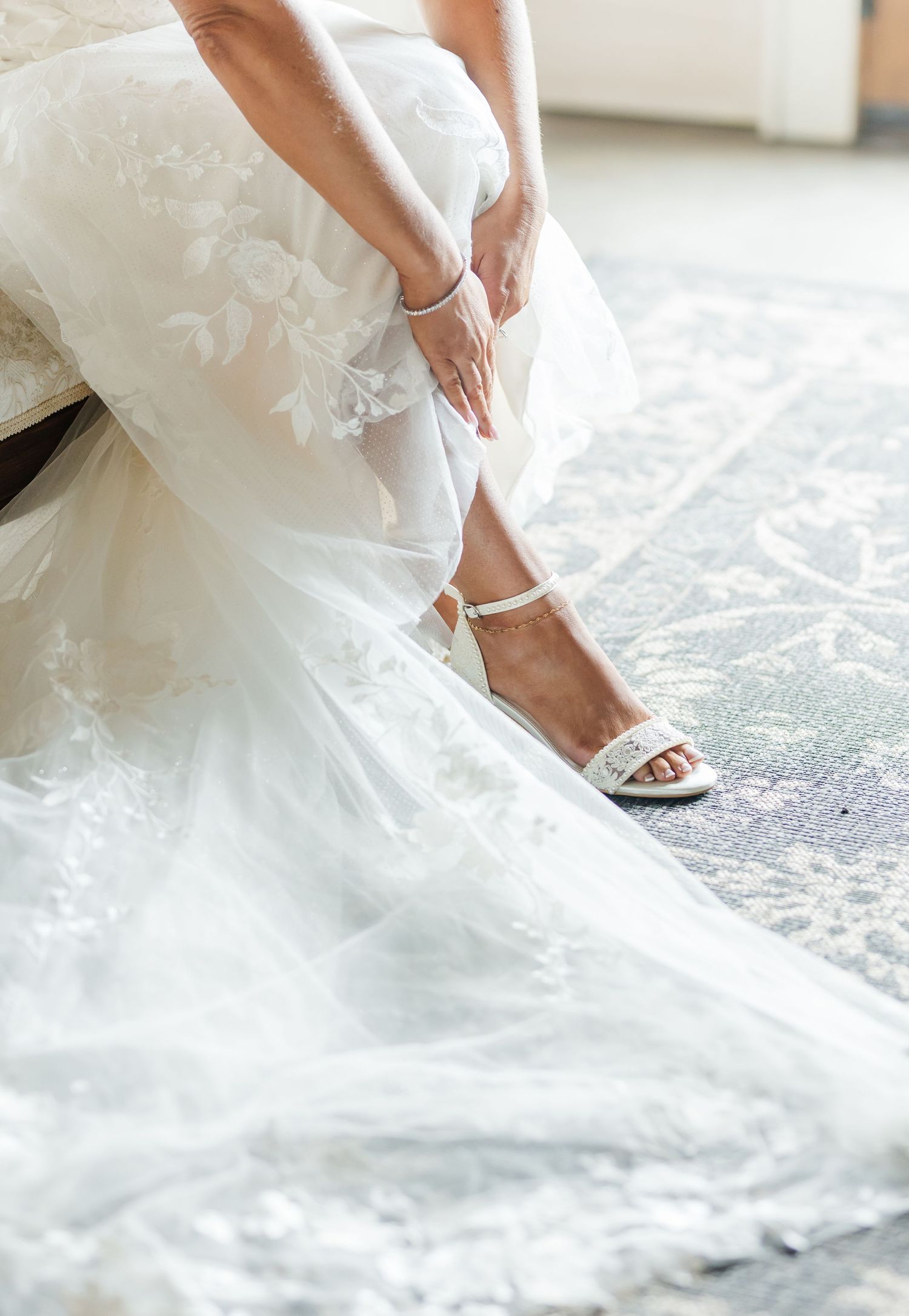 Close-up view of white wedding dress hem and elegant bridal shoes against a light floor.