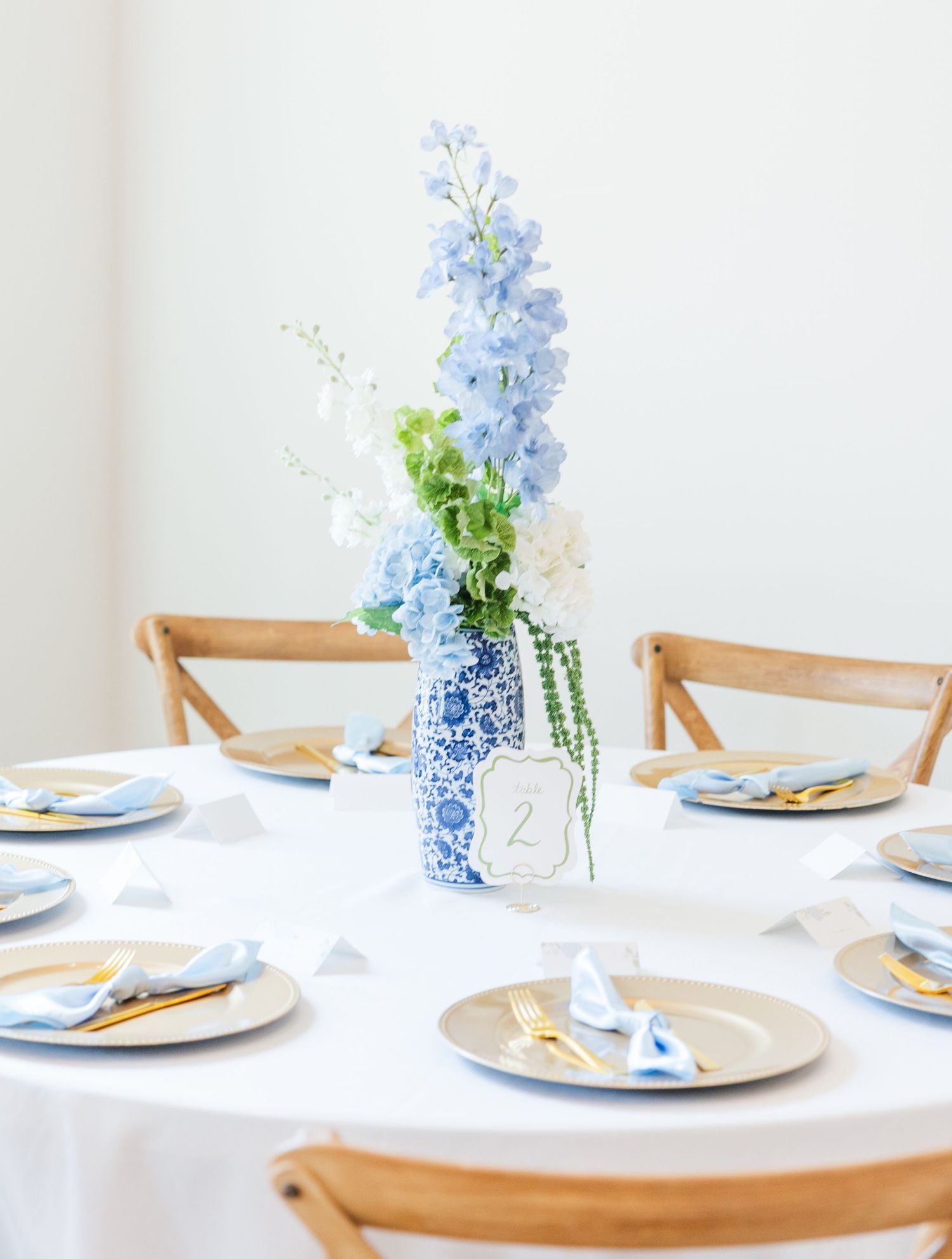 Blue and white chinoiserie vase centerpiece with blue delphinium on a white linen wedding table.