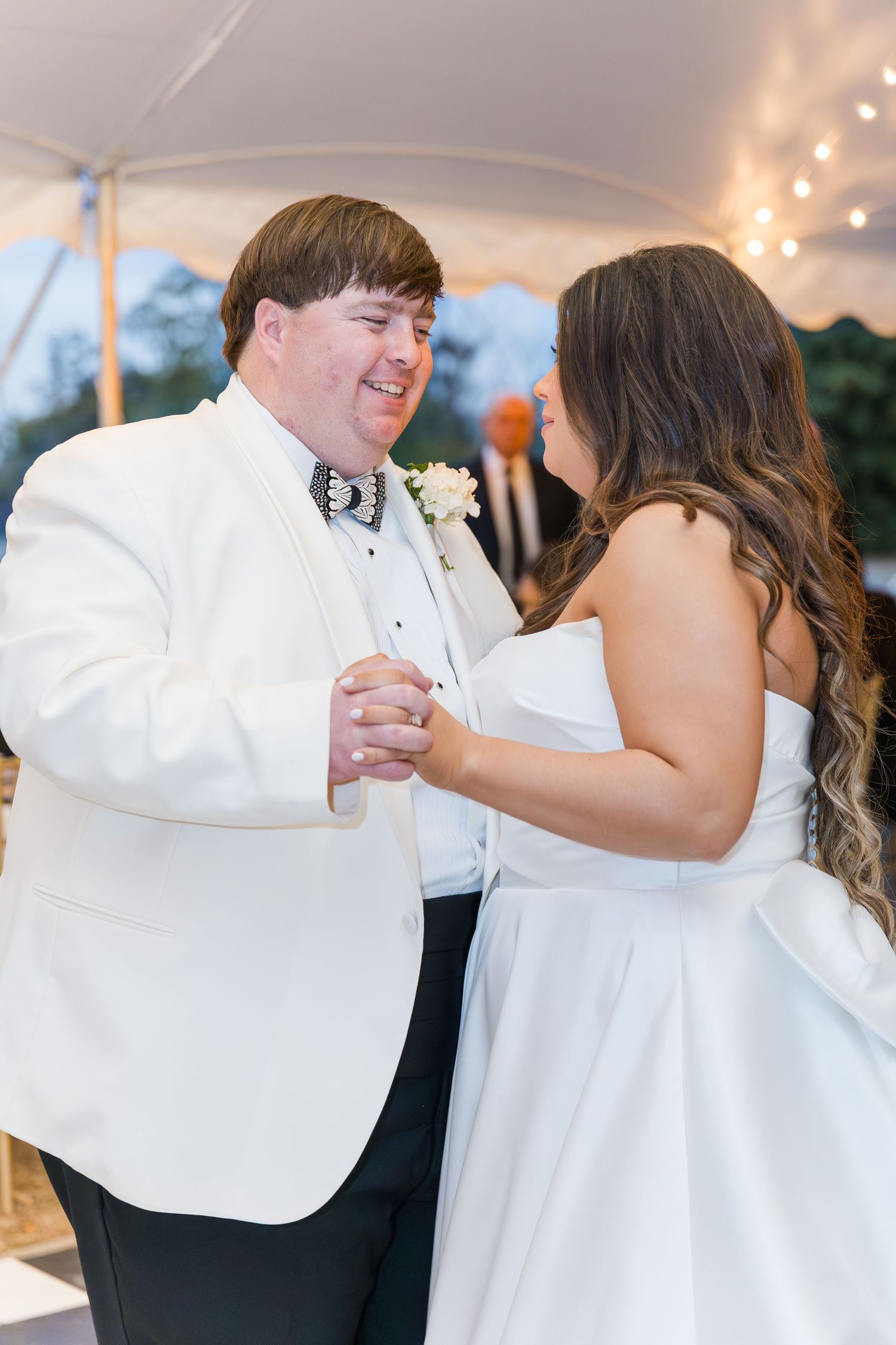 Bride and groom share joyful first dance under tented reception with string lights at wedding.