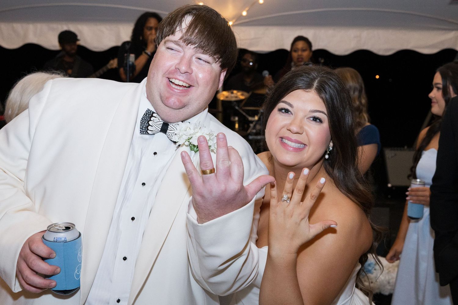 Newlyweds show off wedding rings while celebrating at outdoor tent reception after ceremony.
