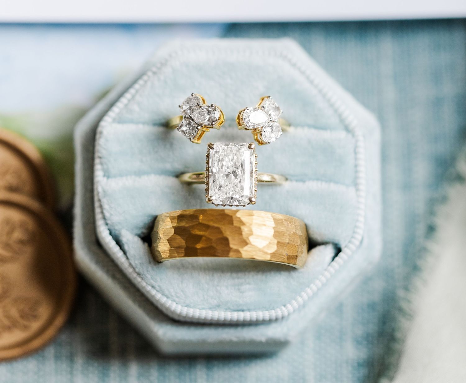 Three gold diamond rings displayed in a blue velvet octagonal jewelry box, featuring elegant engagement and wedding bands.