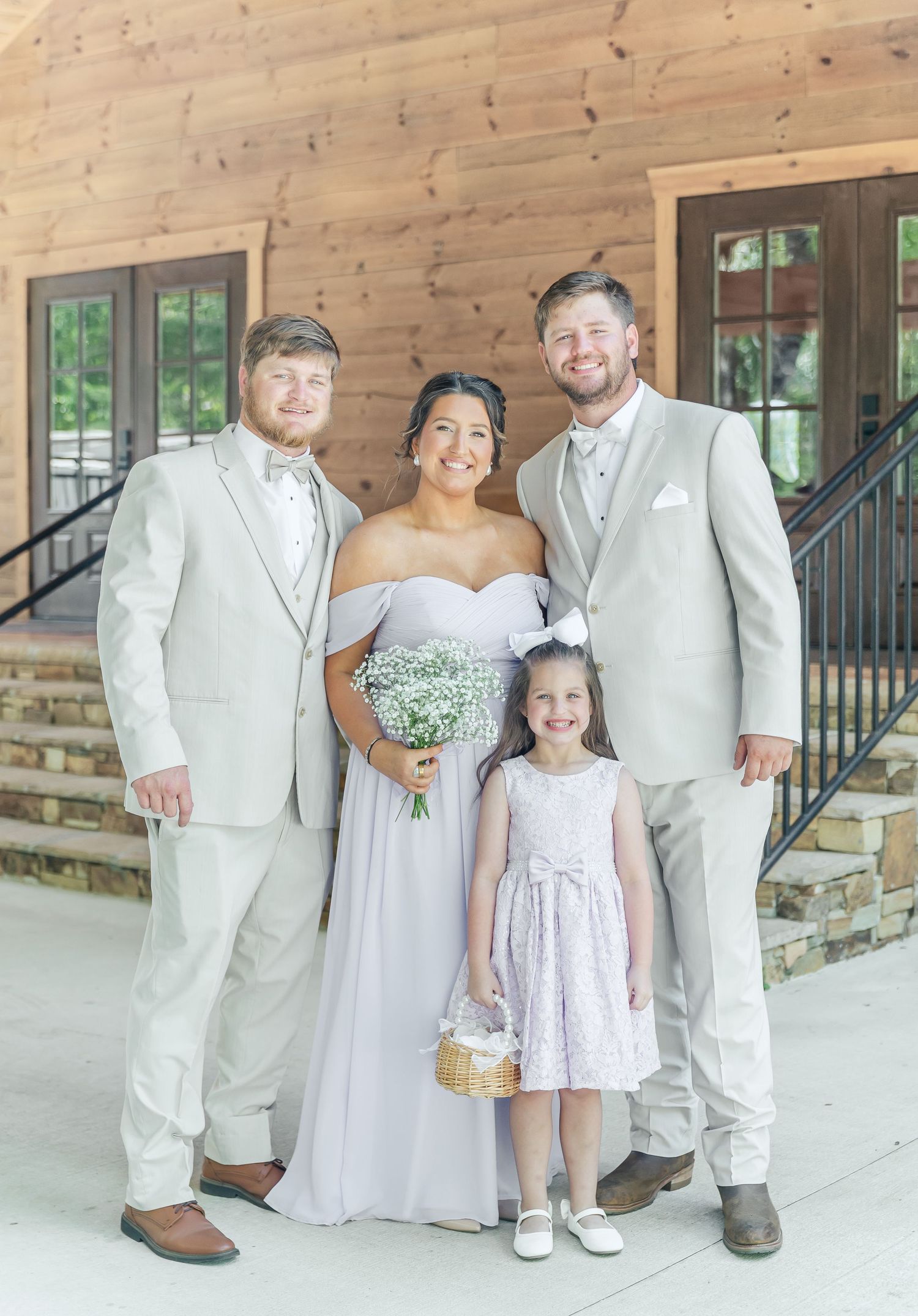 Wedding party poses together on rustic porch with flower girl in white dress holding basket.