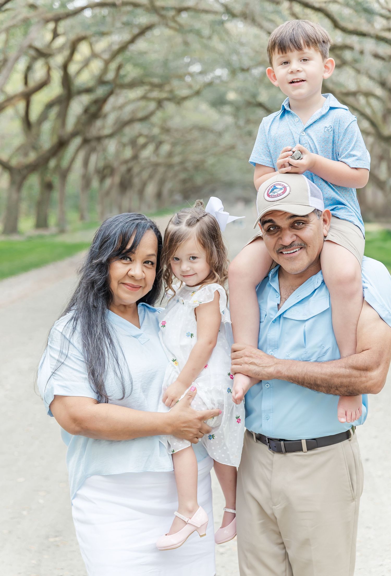 Family of four poses together on a scenic path with overhanging oak trees.