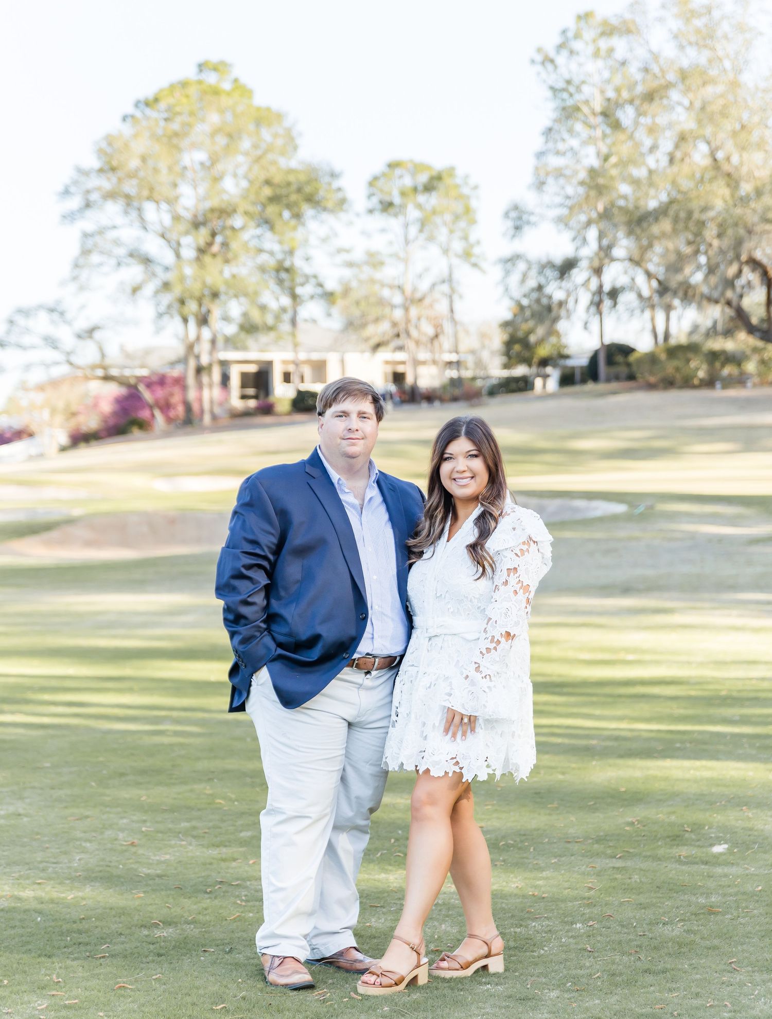 Engaged couple posing together on a golf course lawn.