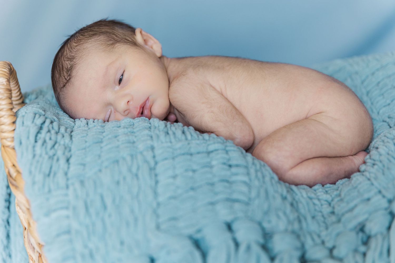 Newborn baby sleeping peacefully on soft blue textured blanket.