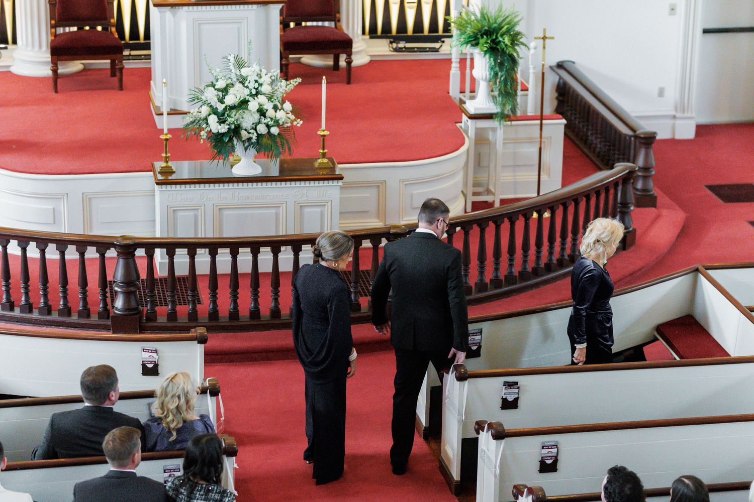 Aerial view of wedding guests and officiant gathered near church altar with red carpet and white floral arrangements.